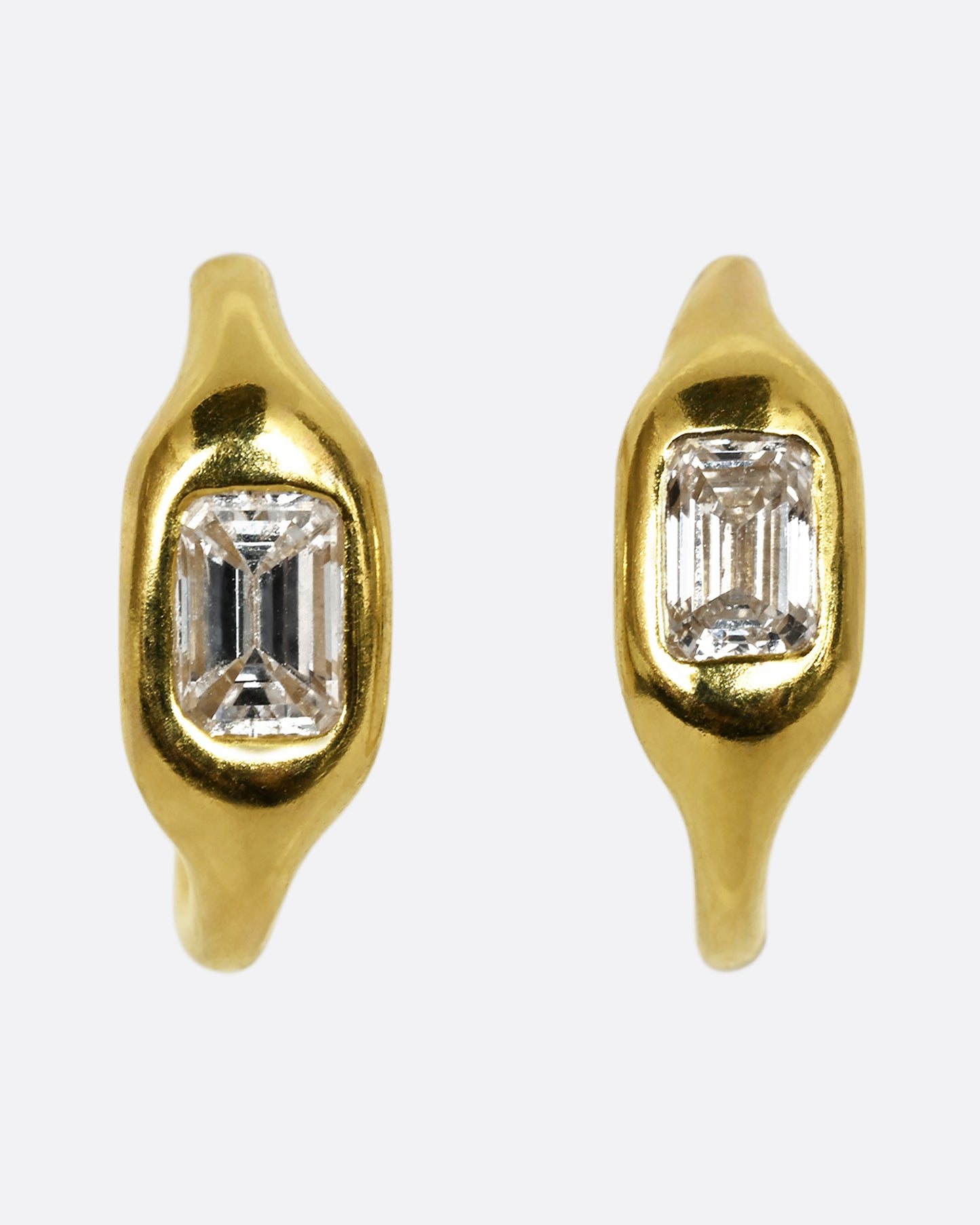 A yellow gold hoop with a single baguette diamond. Shown from the front along side another.