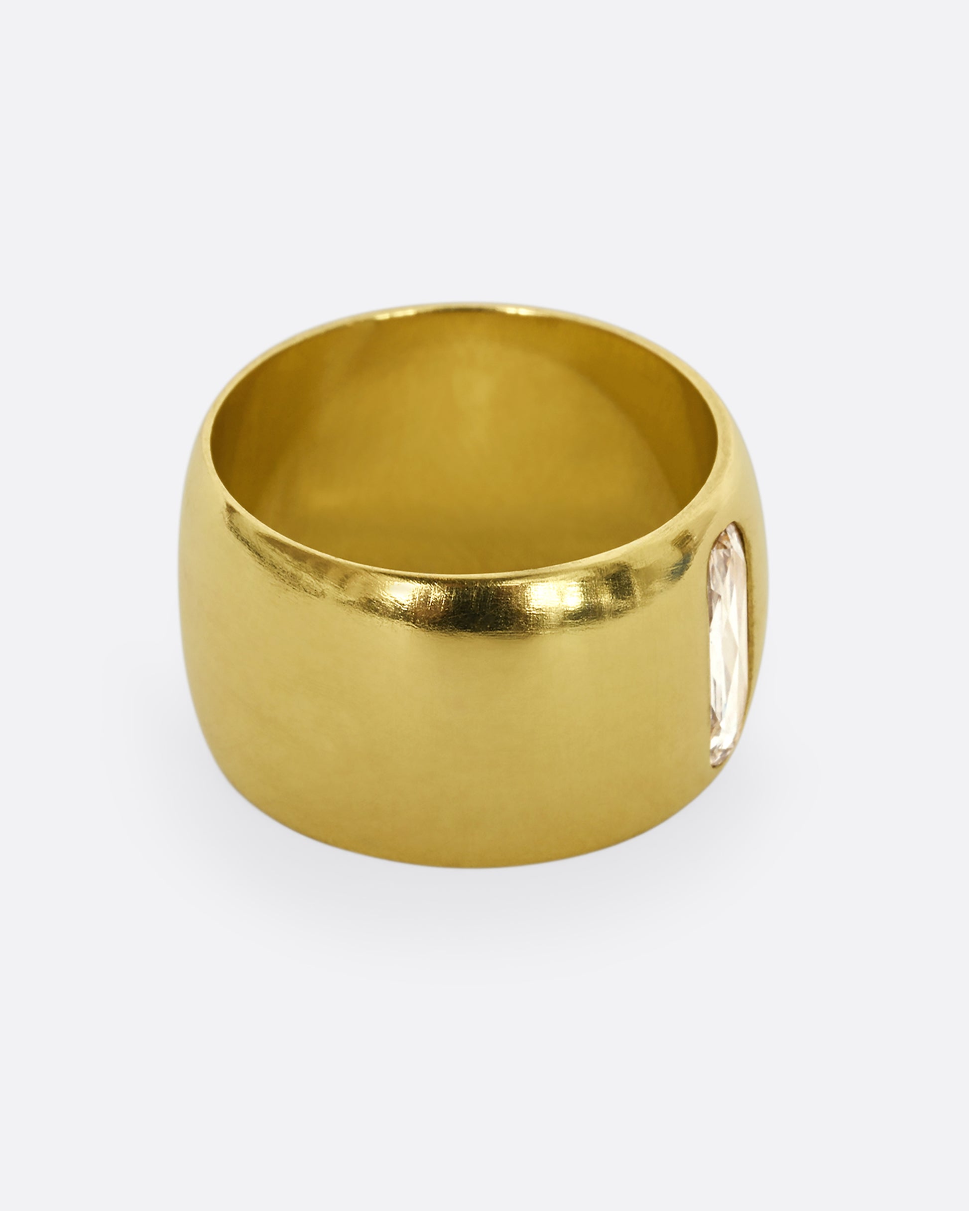 A yellow gold cigar band with an oval shaped diamond. Shown from the side.