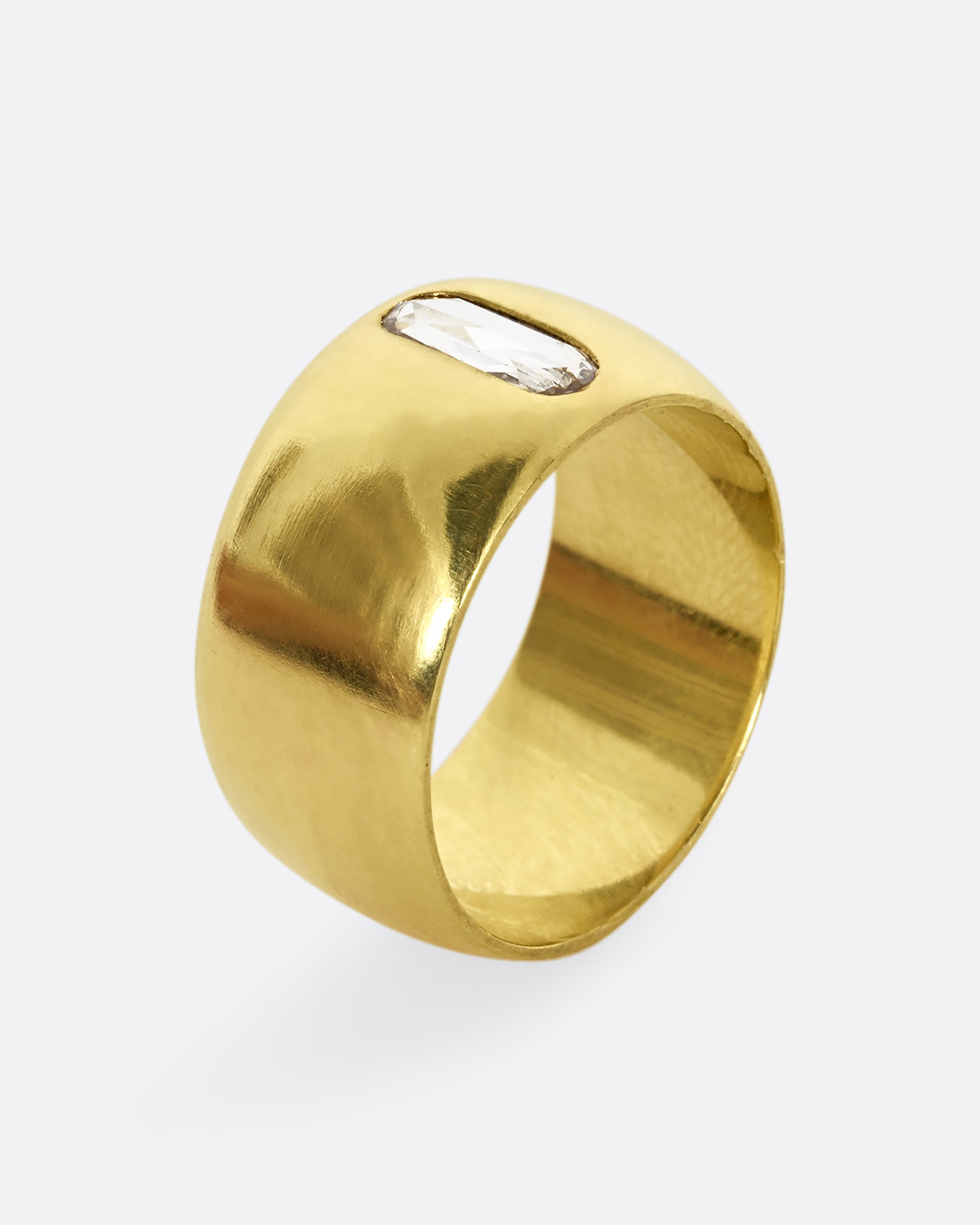 A yellow gold cigar band with an oval shaped diamond. Shown from the side, standing up.