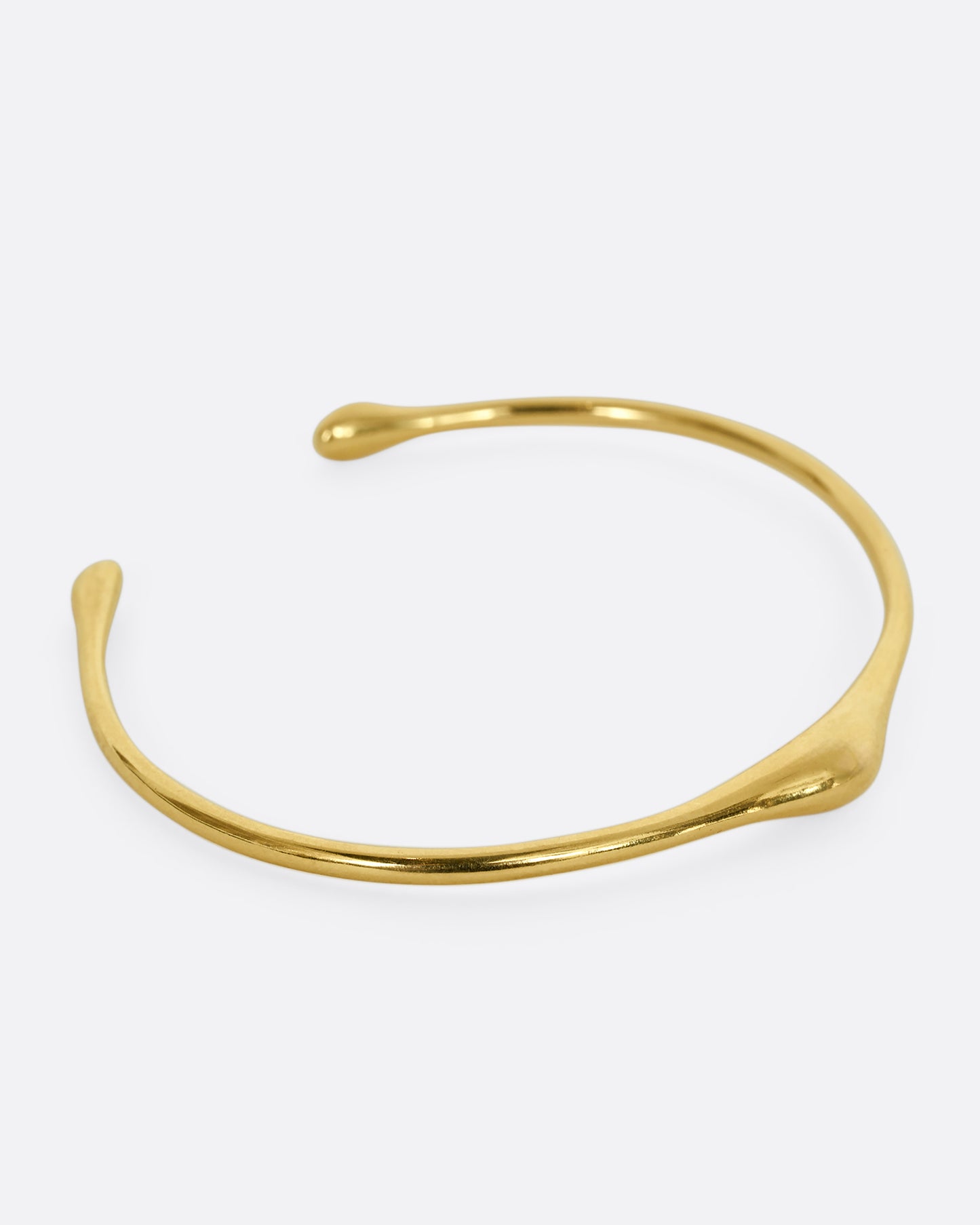 A yellow gold cuff bracelet with a bump. Shown from the side.