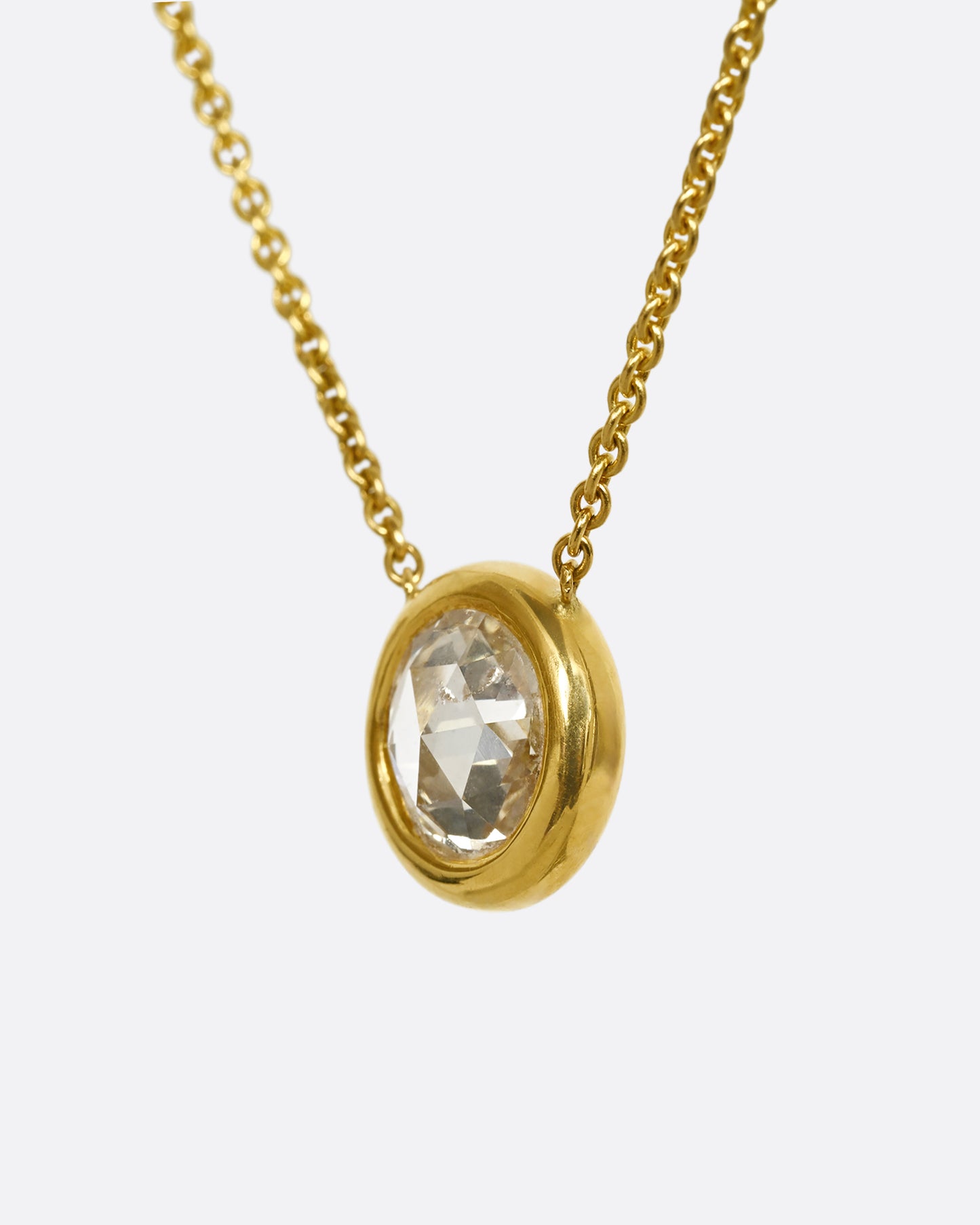 A yellow gold necklace with a circular shaped rose cut diamond. Shown from the side.