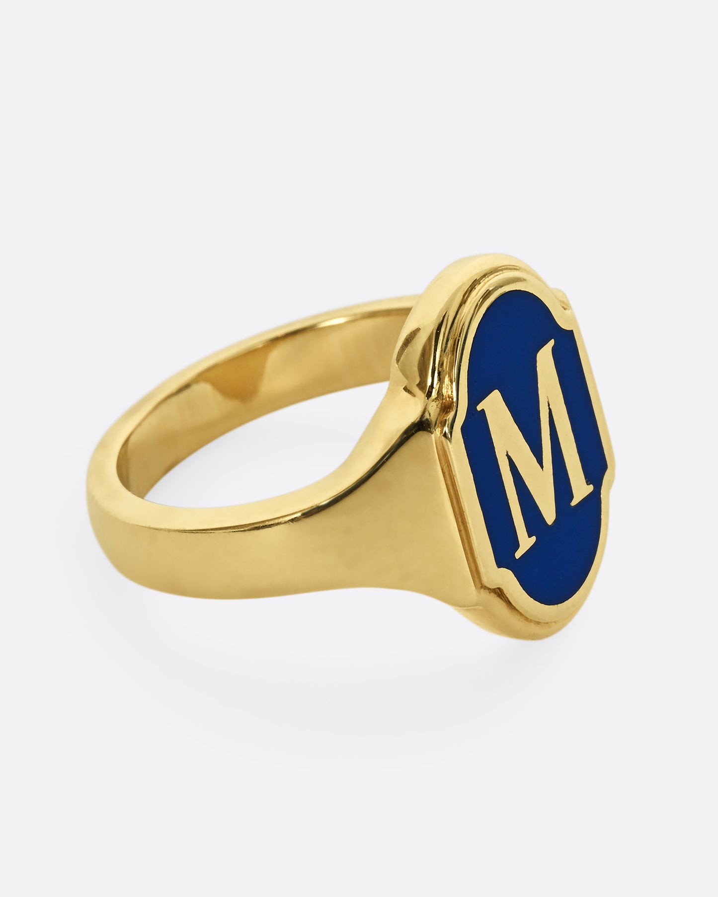 A yellow gold signet ring with blue enamel and the letter "M". Shown from the side.