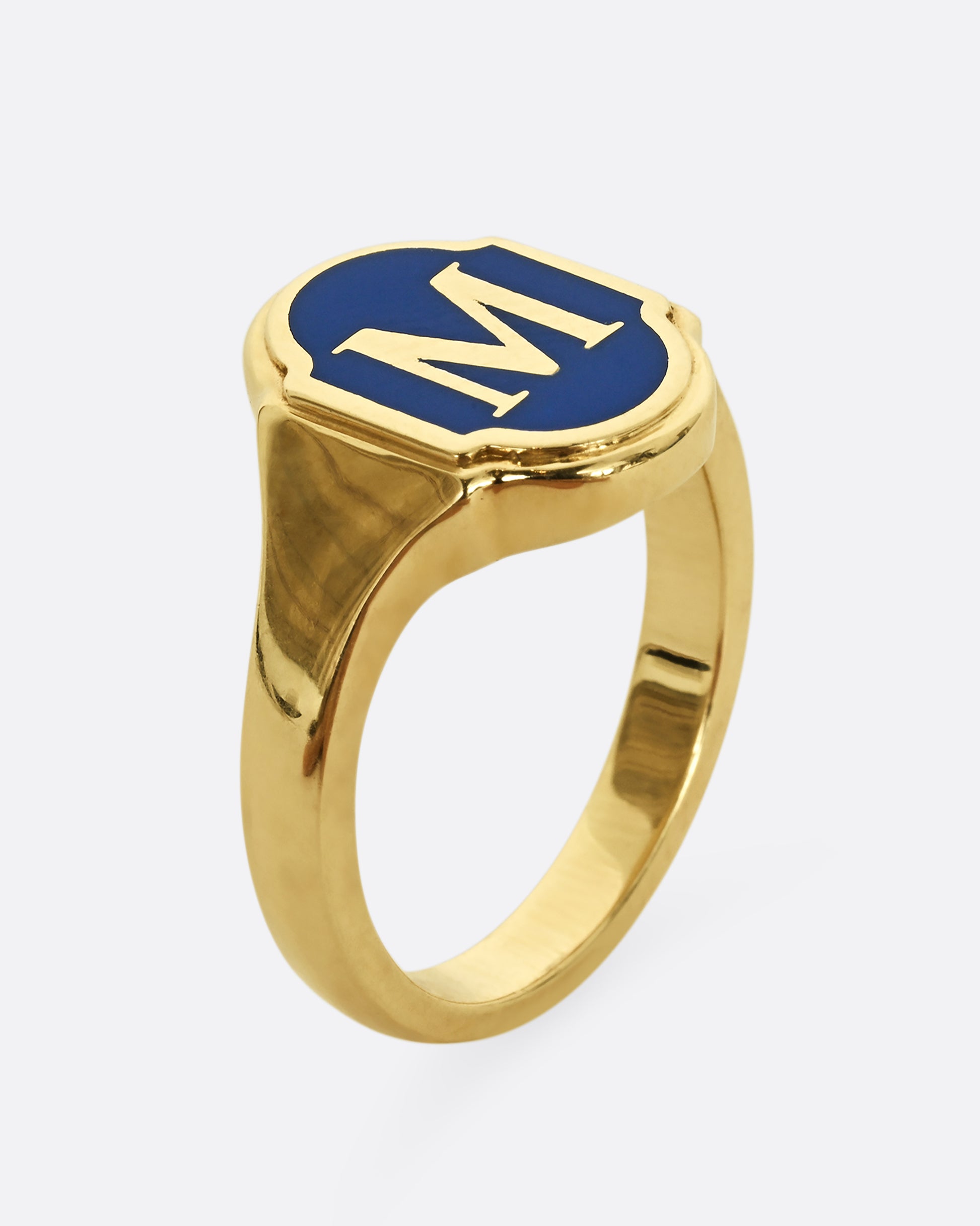 A yellow gold signet ring with blue enamel and the letter "M". Shown from the side, standing up.