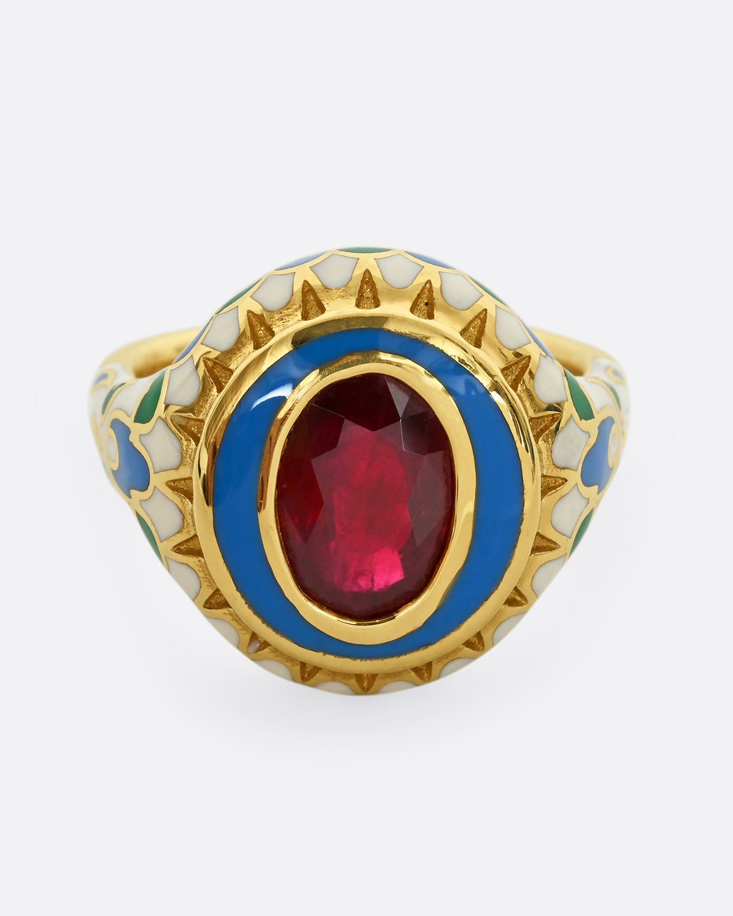 A yellow gold ring with multicolor enamel around an oval shaped ruby. Shown from the front from slightly above.