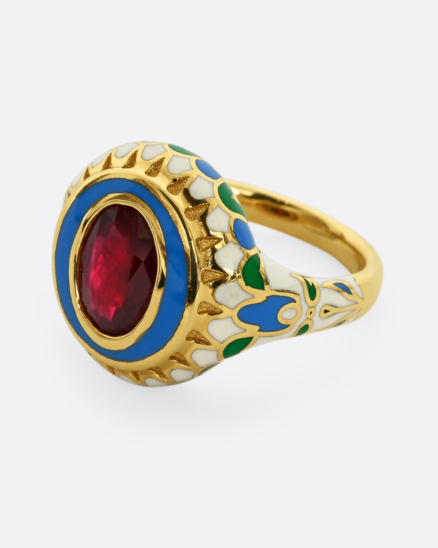 A yellow gold ring with multicolor enamel around an oval shaped ruby. Shown from the side.