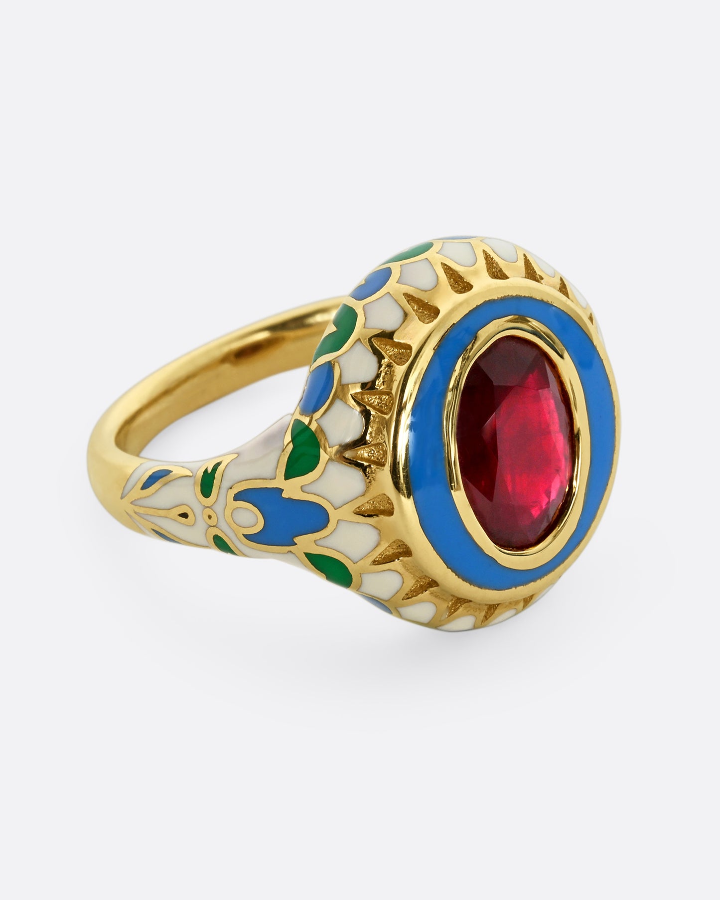 A yellow gold ring with multicolor enamel around an oval shaped ruby. Shown from the side.