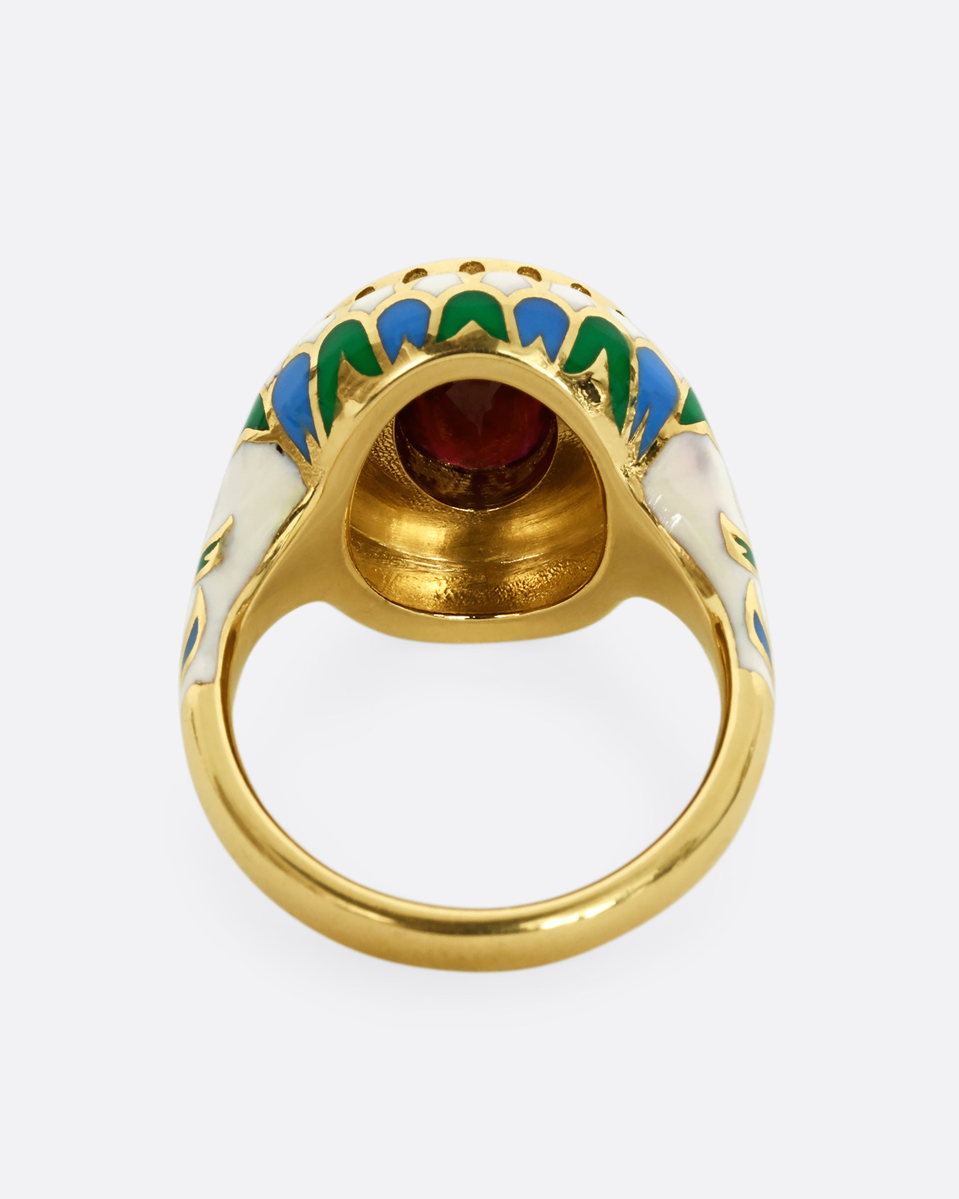 A yellow gold ring with multicolor enamel around an oval shaped ruby. Shown from the back.