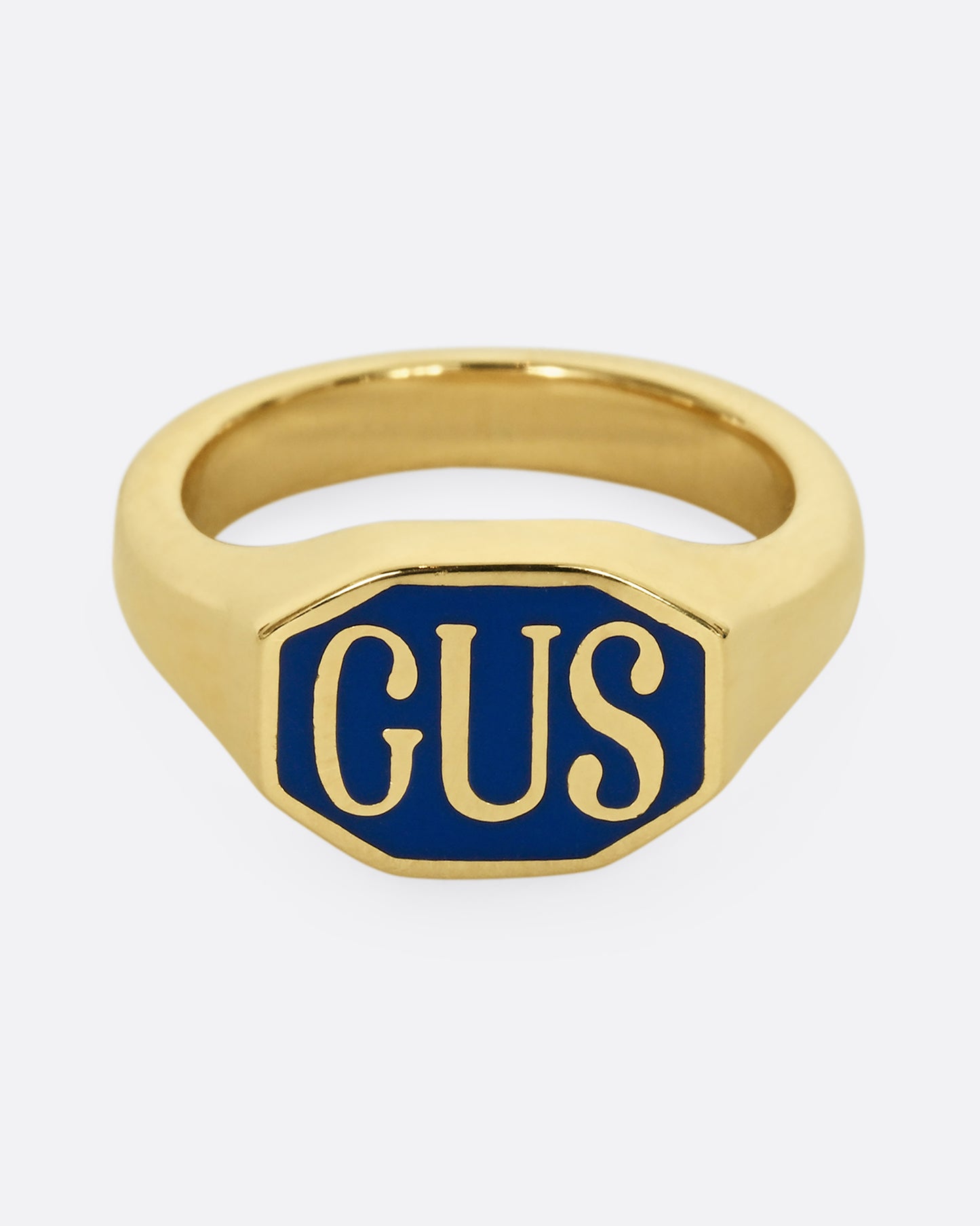 A yellow gold signet ring with the initials "GUS" and blue enamel. Shown from the front.