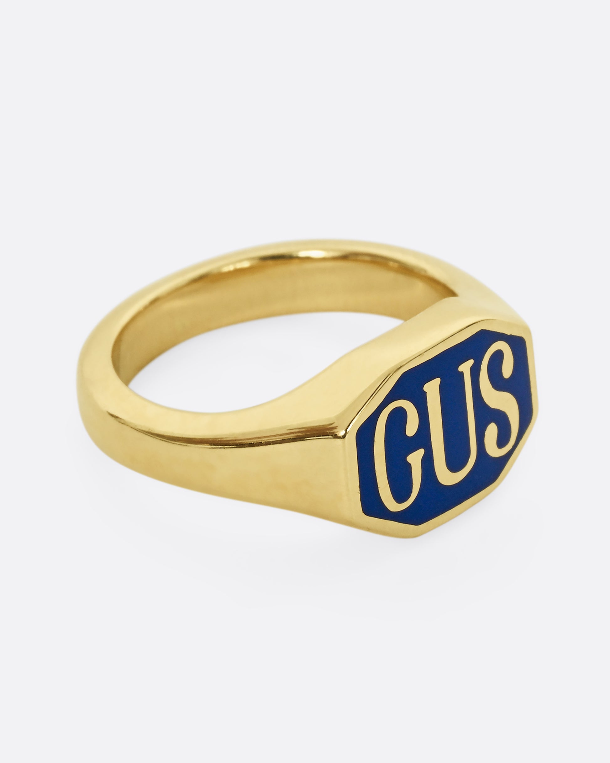 A yellow gold signet ring with the initials "GUS" and blue enamel. Shown from the side.