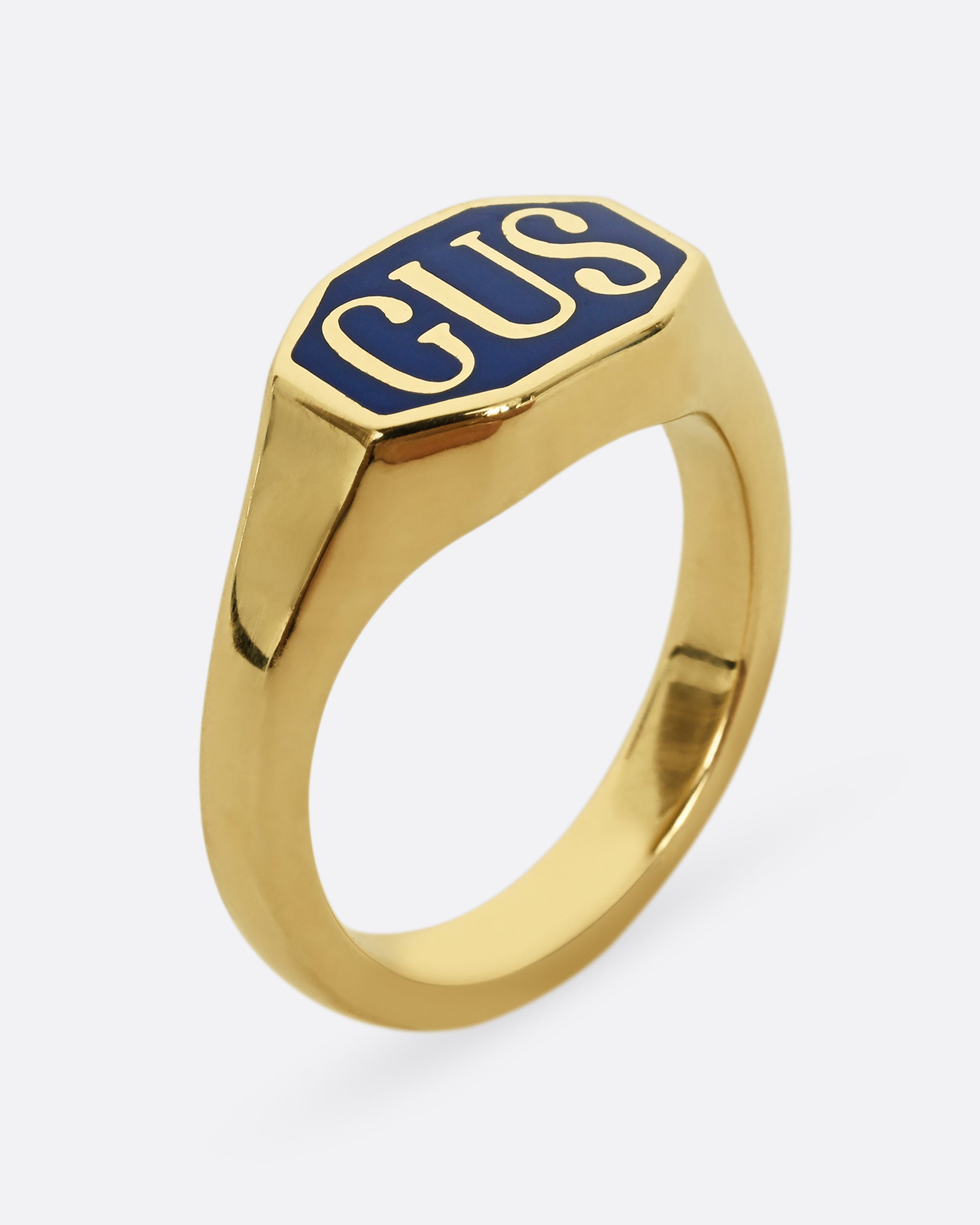 A yellow gold signet ring with the initials "GUS" and blue enamel. Shown from the side, standing up. 