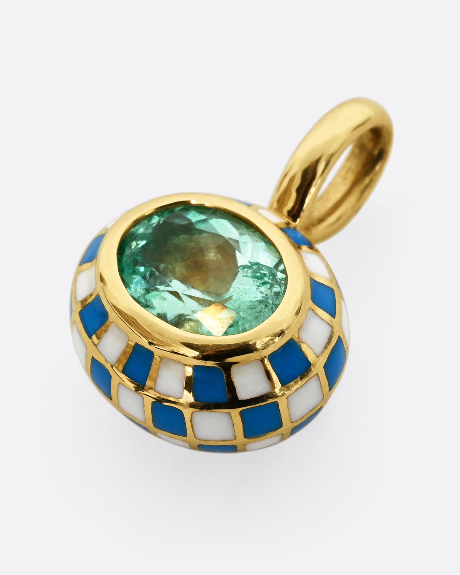 A yellow gold oval pendant with blue and white enamel surrounding an emerald. Shown laying flat.