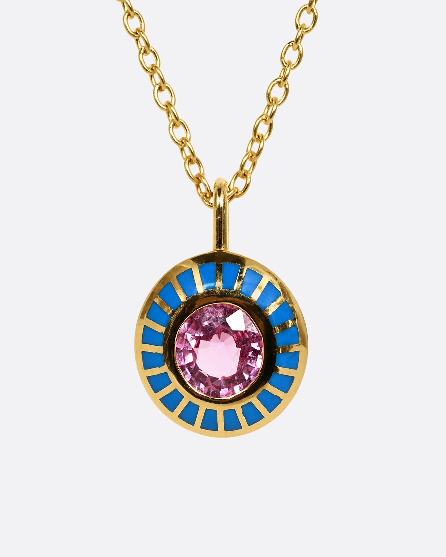 A yellow gold pendant with light blue enamel surrounding a pink sapphire. Shown on a cable chain from the front, close up.