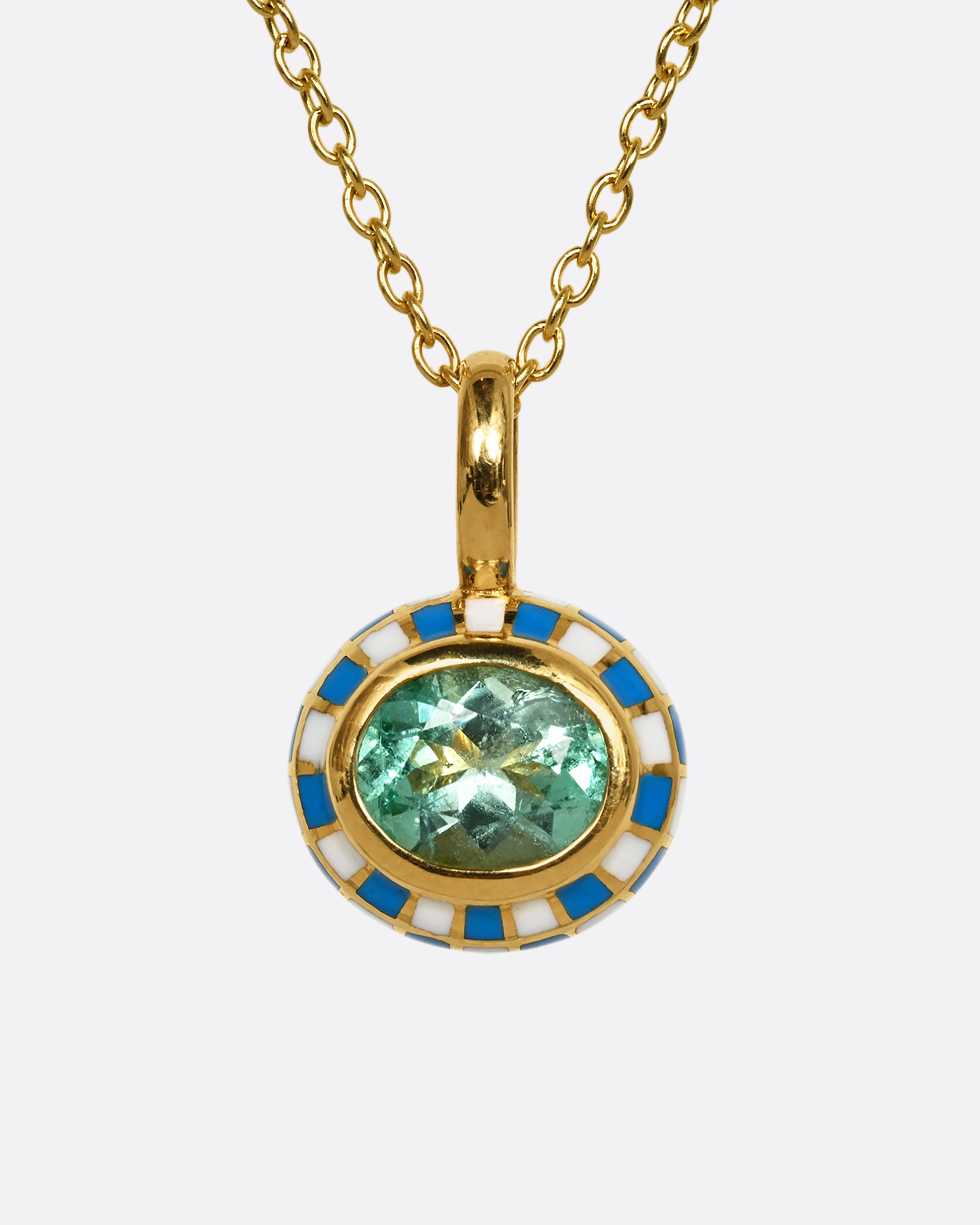 A yellow gold oval pendant with blue and white enamel surrounding an emerald. Shown hanging from a cable chain, from the front.