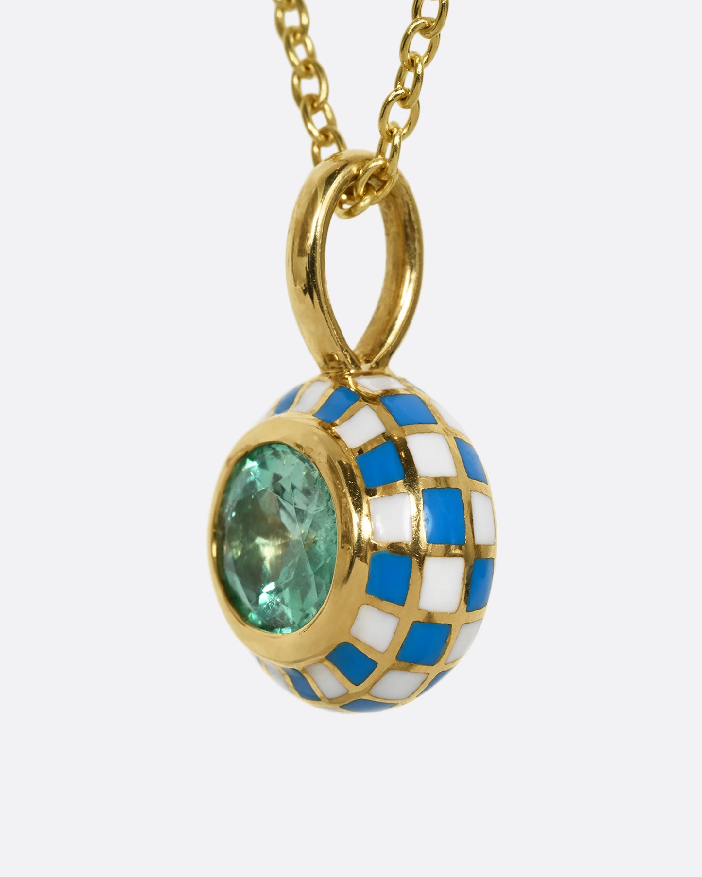 A yellow gold oval pendant with blue and white enamel surrounding an emerald. Shown hanging from a cable chain from the side.