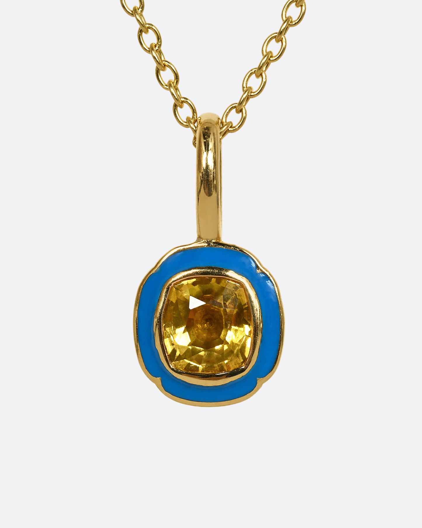 A yellow gold pendant with blue enamel surrounding a cushion cut yellow sapphire. Shown from the front.