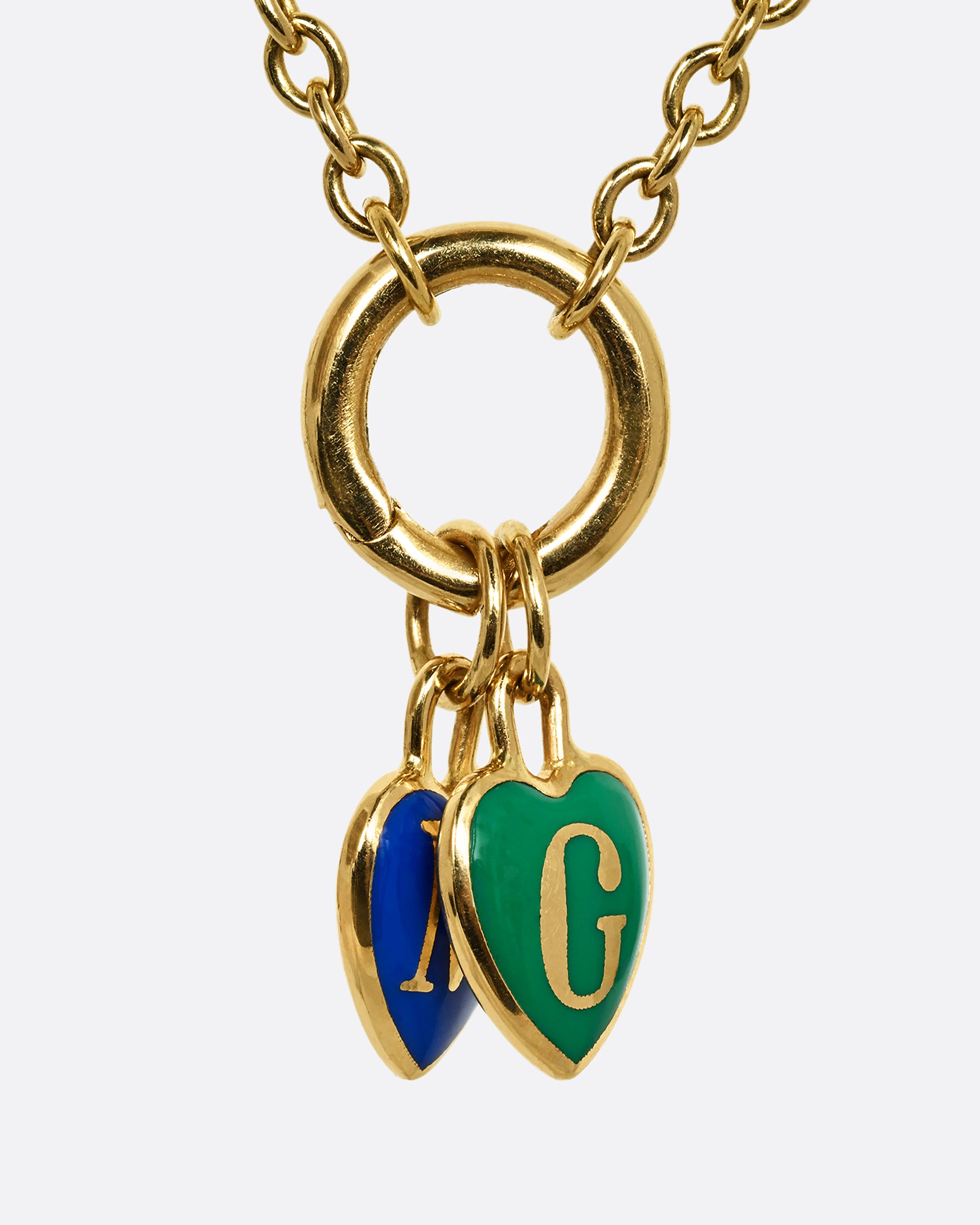 A yellow gold letter "G" heart shaped charm with green enamel. Shown on a chain styled with other charms on a charm holder.