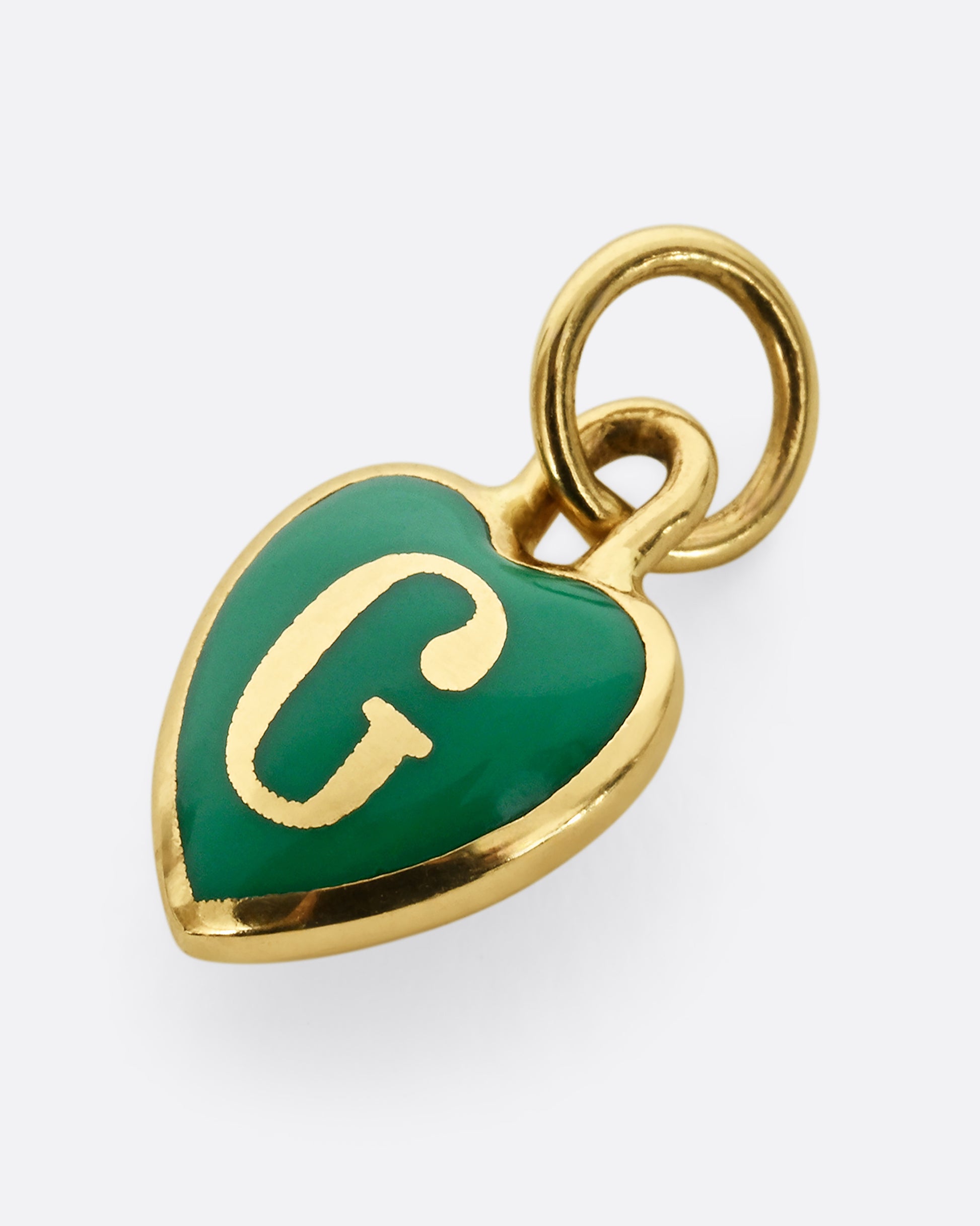 A yellow gold letter "G" heart shaped charm with green enamel. Shown laying flat.