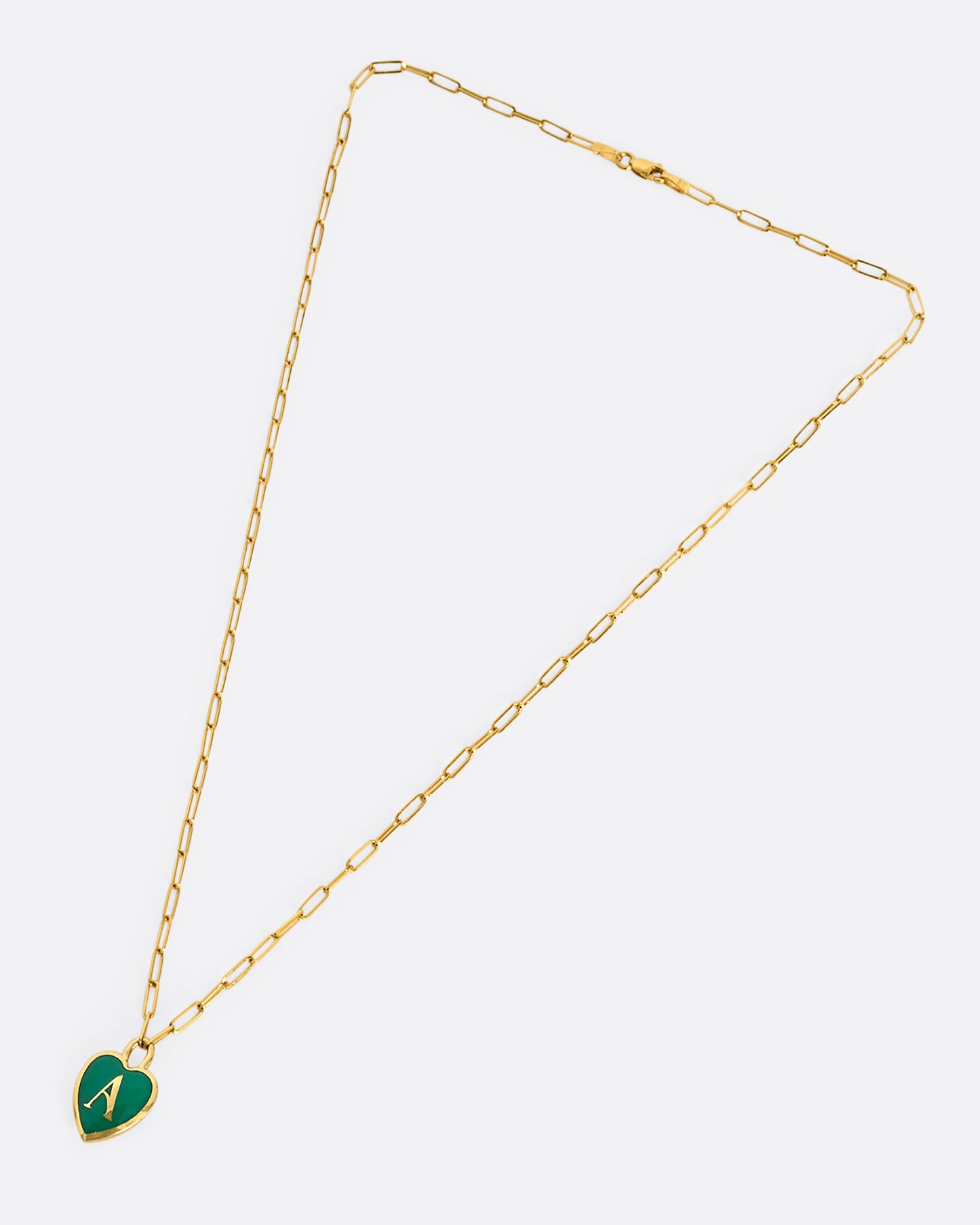 A yellow gold paper clip chain necklace with a heart shaped pendant that has green enamel and the letter "A". Shown from above, laying flat.