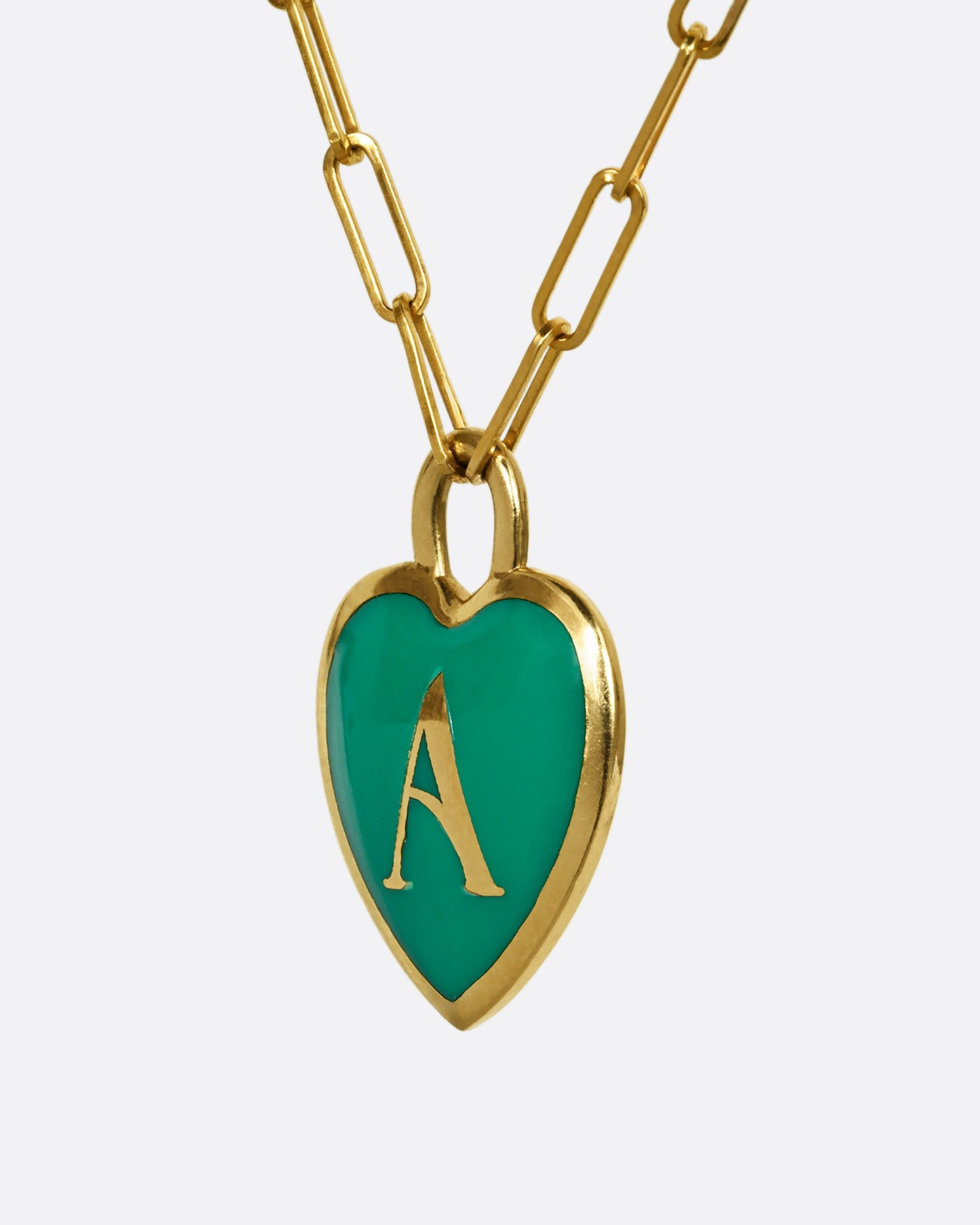 A yellow gold paper clip chain necklace with a heart shaped pendant that has green enamel and the letter "A". Shown from the side.