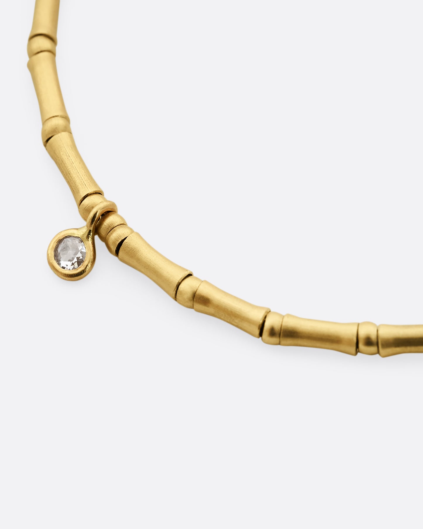 A yellow gold bracelet with tube beads and a single diamond. Shown close up on the diamond.