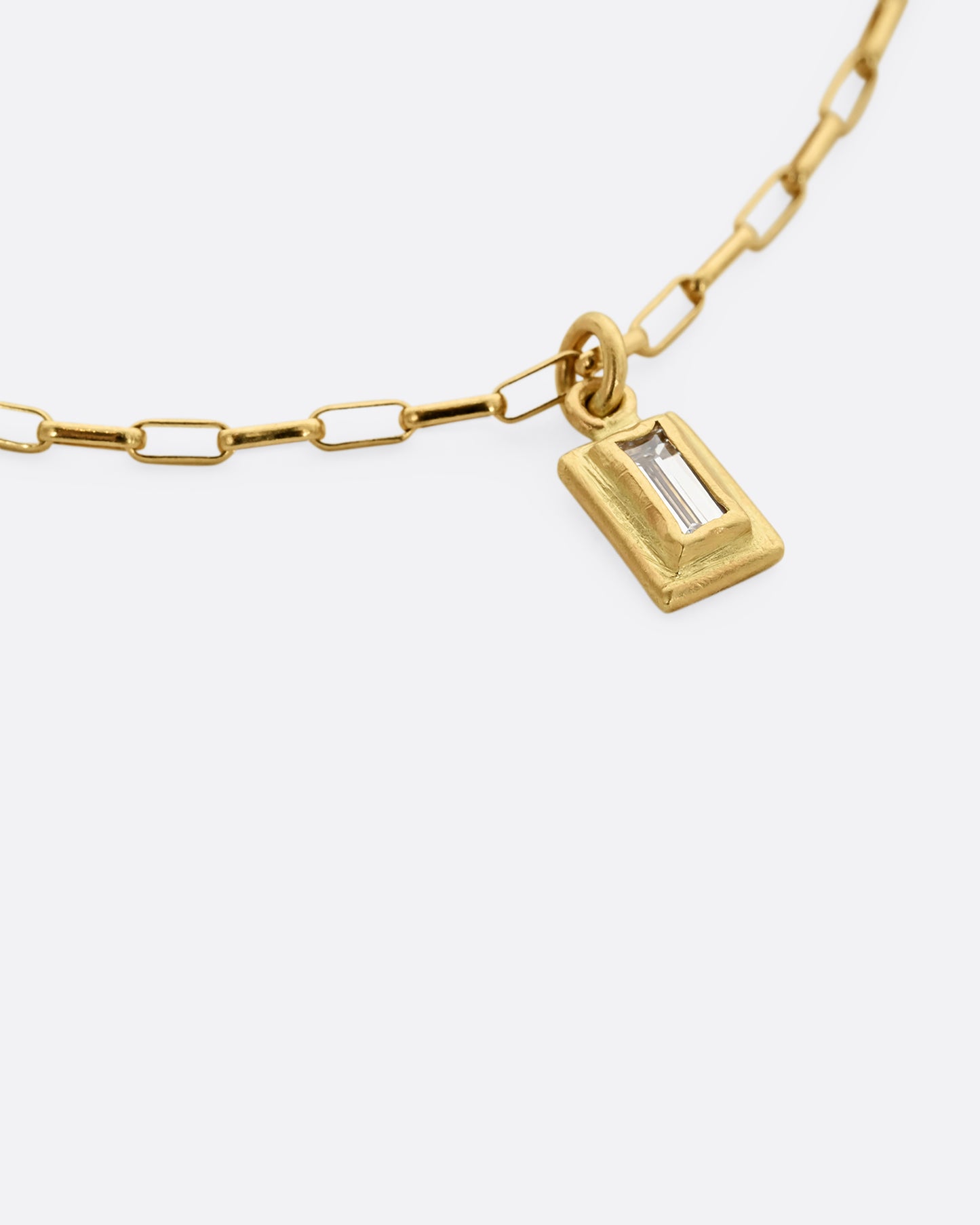 A yellow gold elongated rolo chain bracelet with a baguette diamond. Shown close up on the diamond.