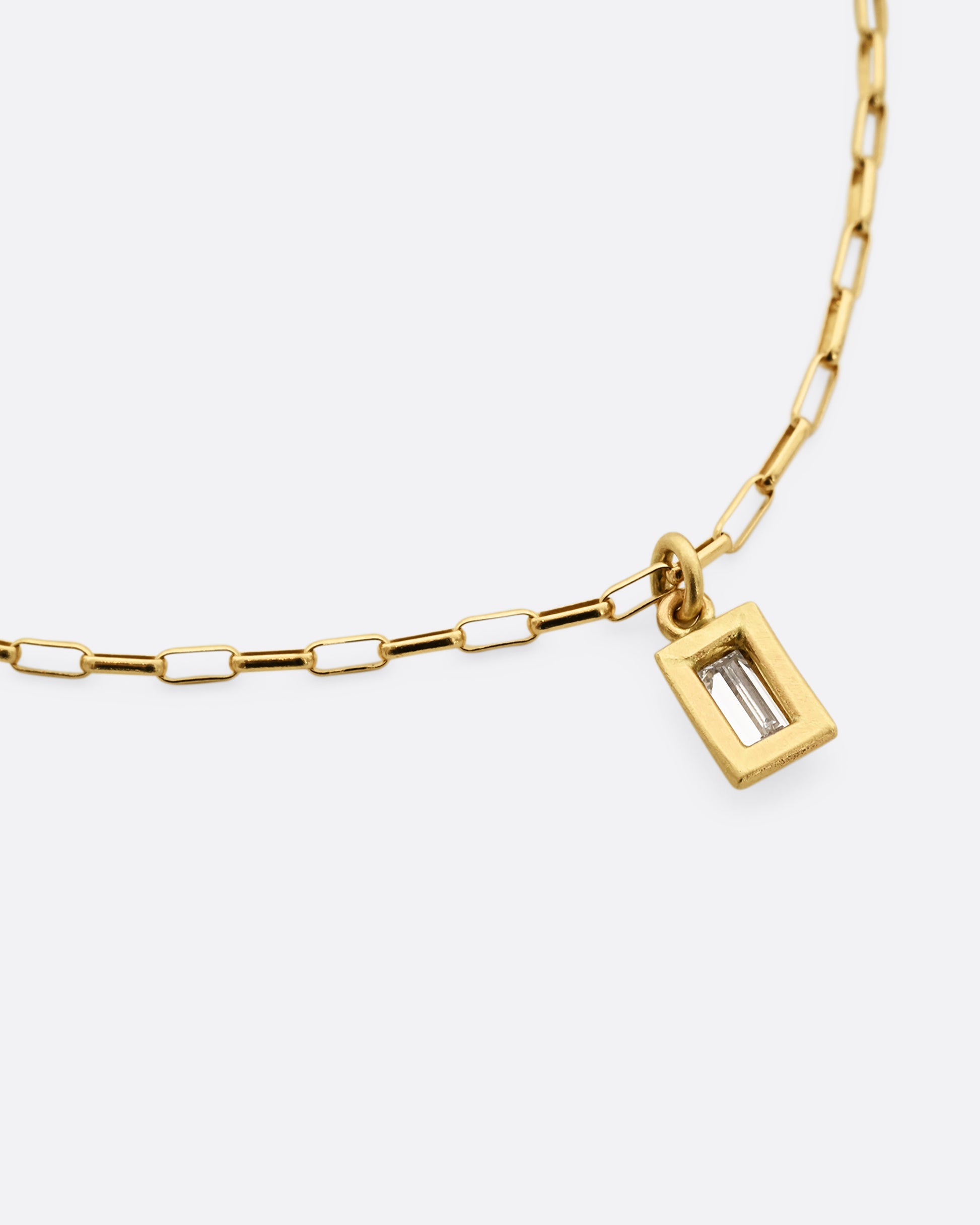 A yellow gold elongated rolo chain bracelet with a baguette diamond. Shown laying flat, backside.