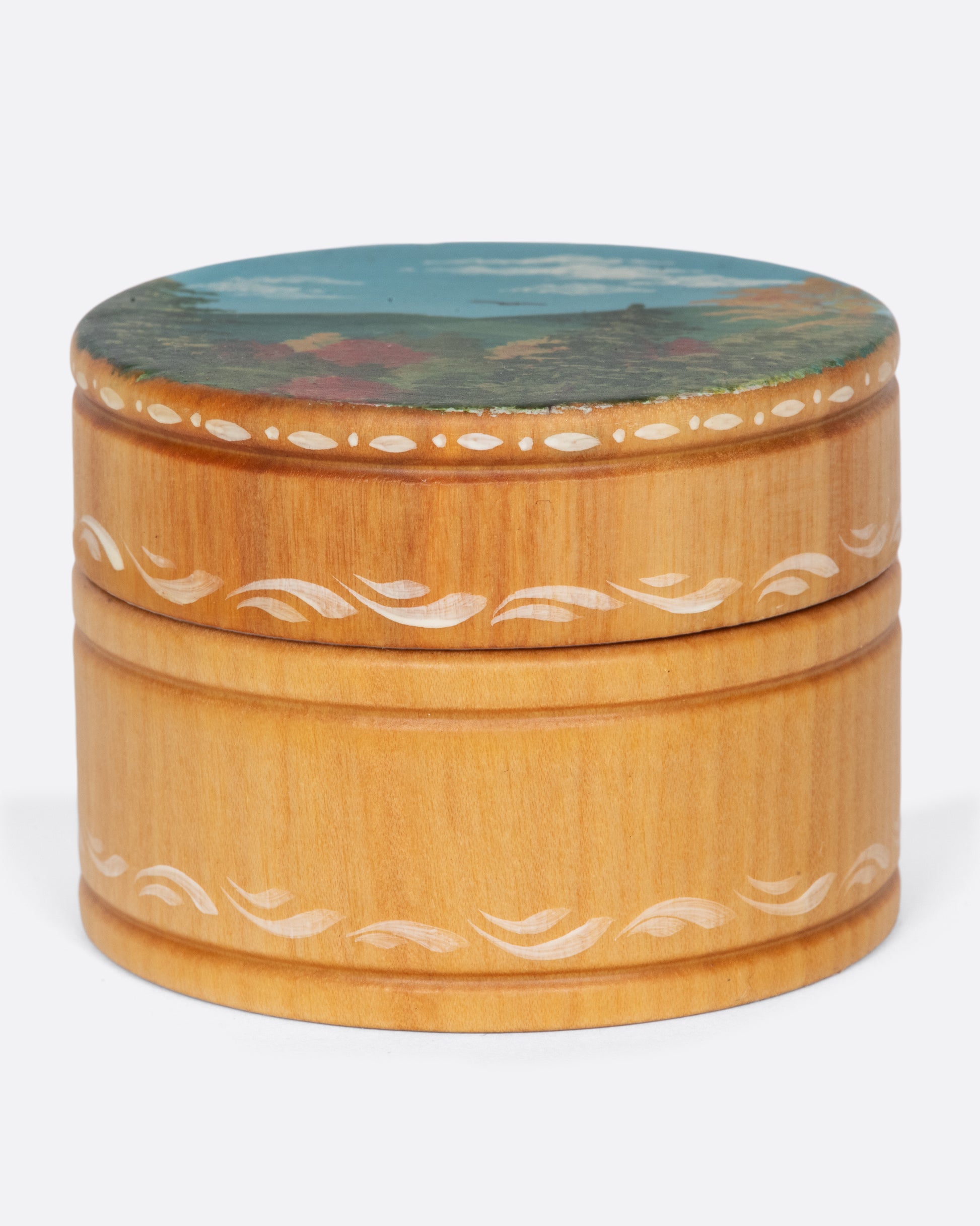 A vintage round wooden box with a beautiful landscape on the lid and painted details around the box.