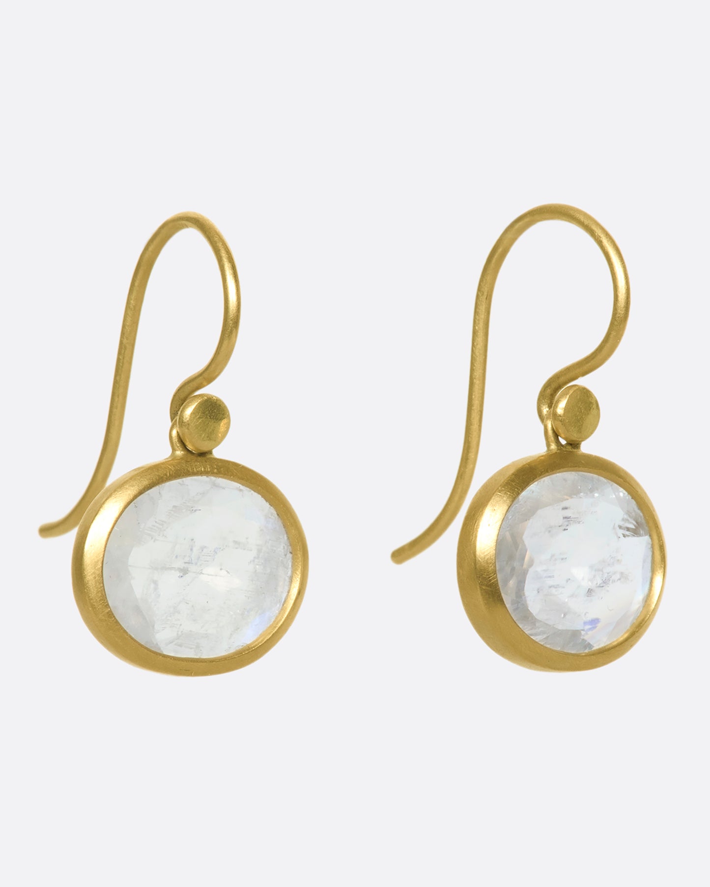A side view of a pair of oval moonstone earrings set in yellow gold bezels.