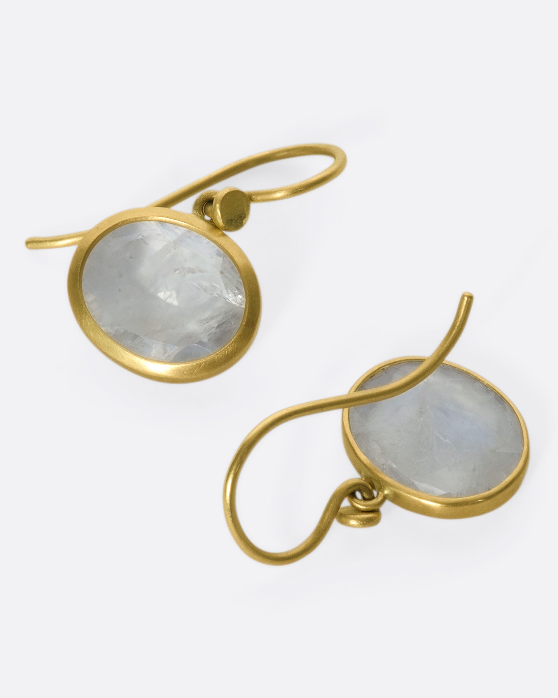 A pair of oval moonstone earrings set in yellow gold bezels, with one laying face up and one laying face down.