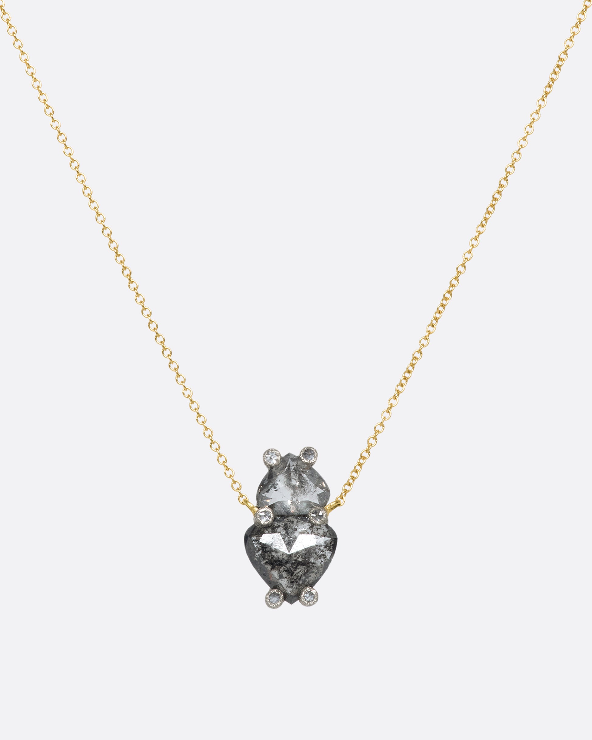 A hanging pendant with two shield cut grey diamonds on a yellow gold chain.