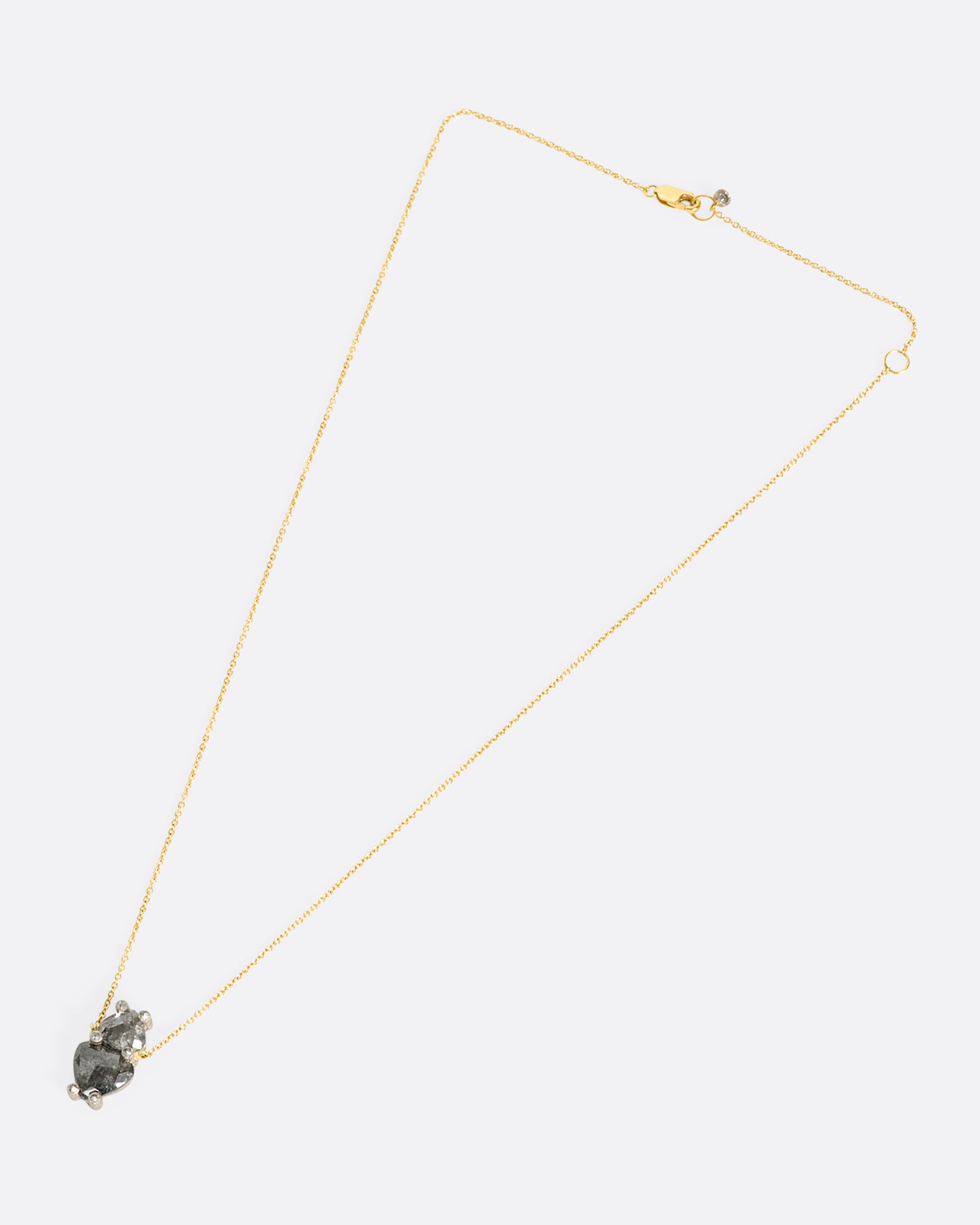An overhead view of a pendant with two shield cut grey diamonds on a yellow gold chain laying down flat.