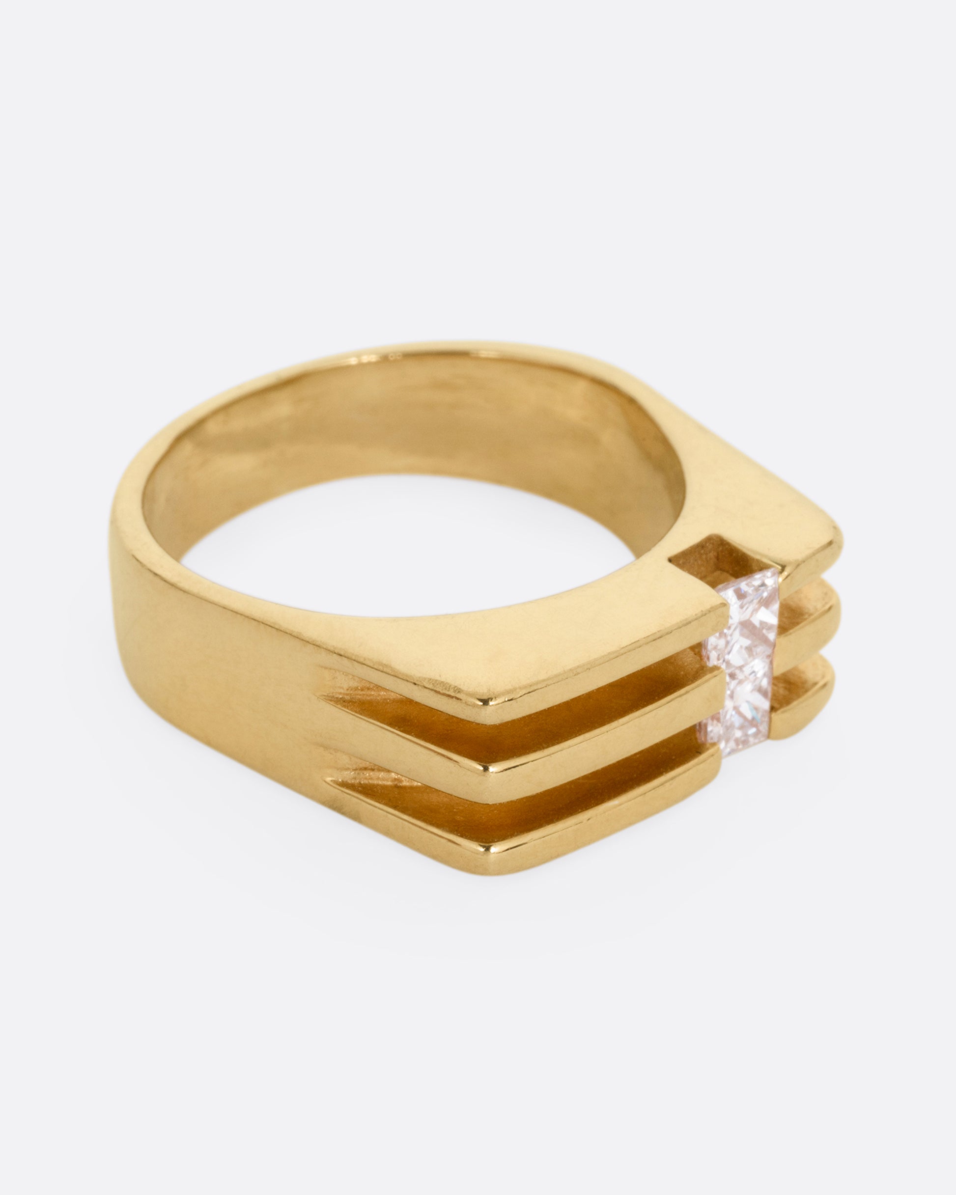 A yellow gold ring with linear channels and two princess cut diamonds, shown from the side. 