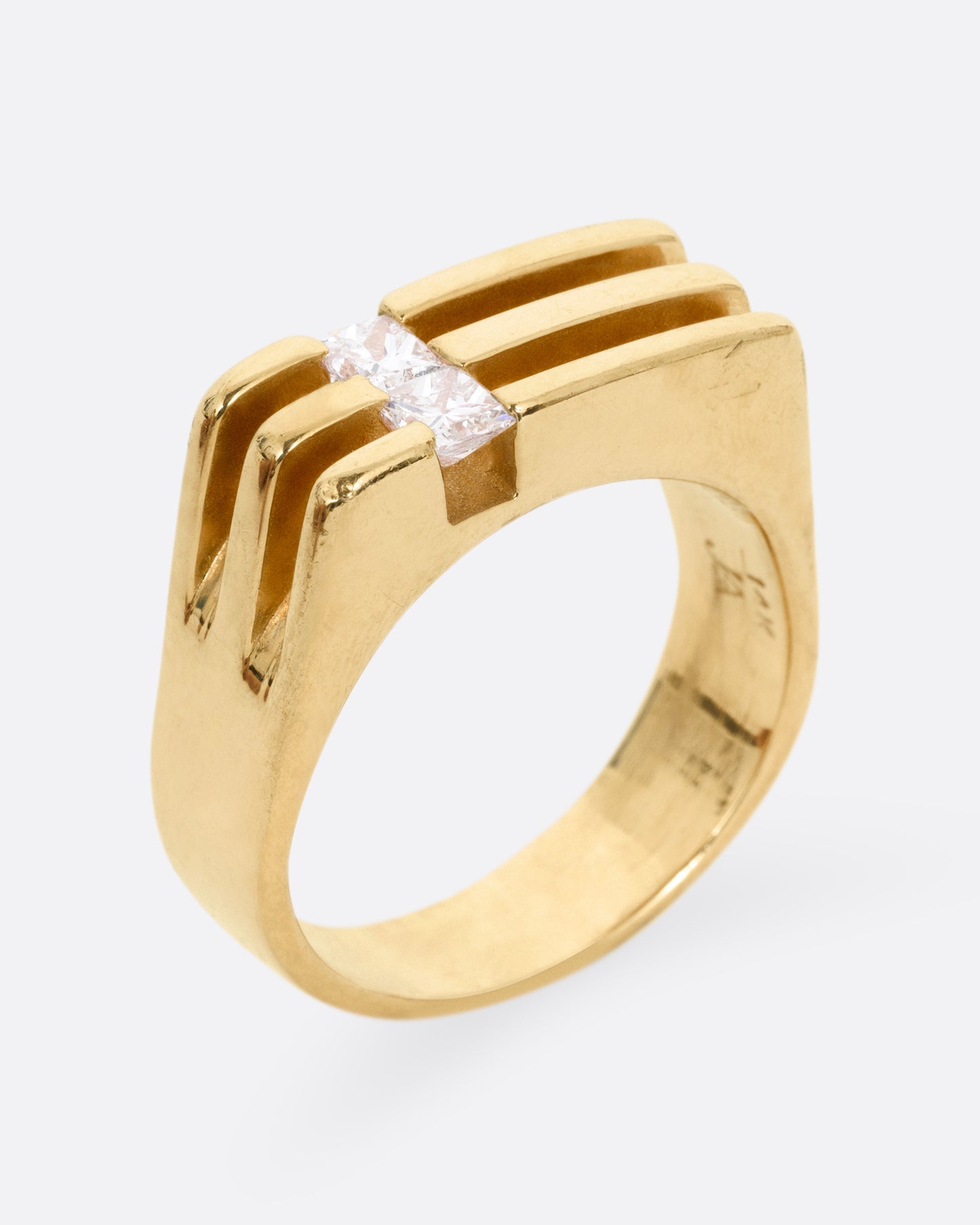 A yellow gold ring with linear channels and two princess cut diamonds, shown from the side standing up. 