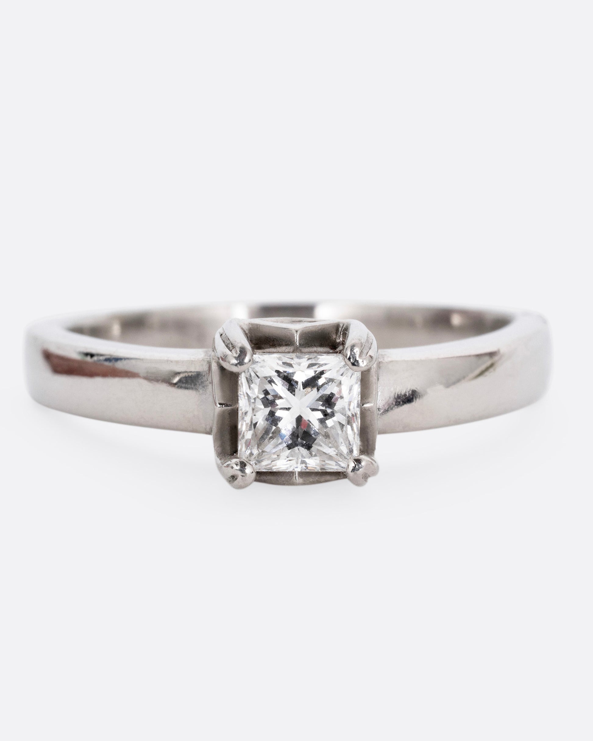 A platinum ring with a princess cut diamond, prong set high above angular cutouts and diamond accents. Shown from the front.