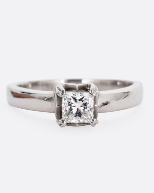 A platinum ring with a princess cut diamond, prong set high above angular cutouts and diamond accents. Shown from the front.