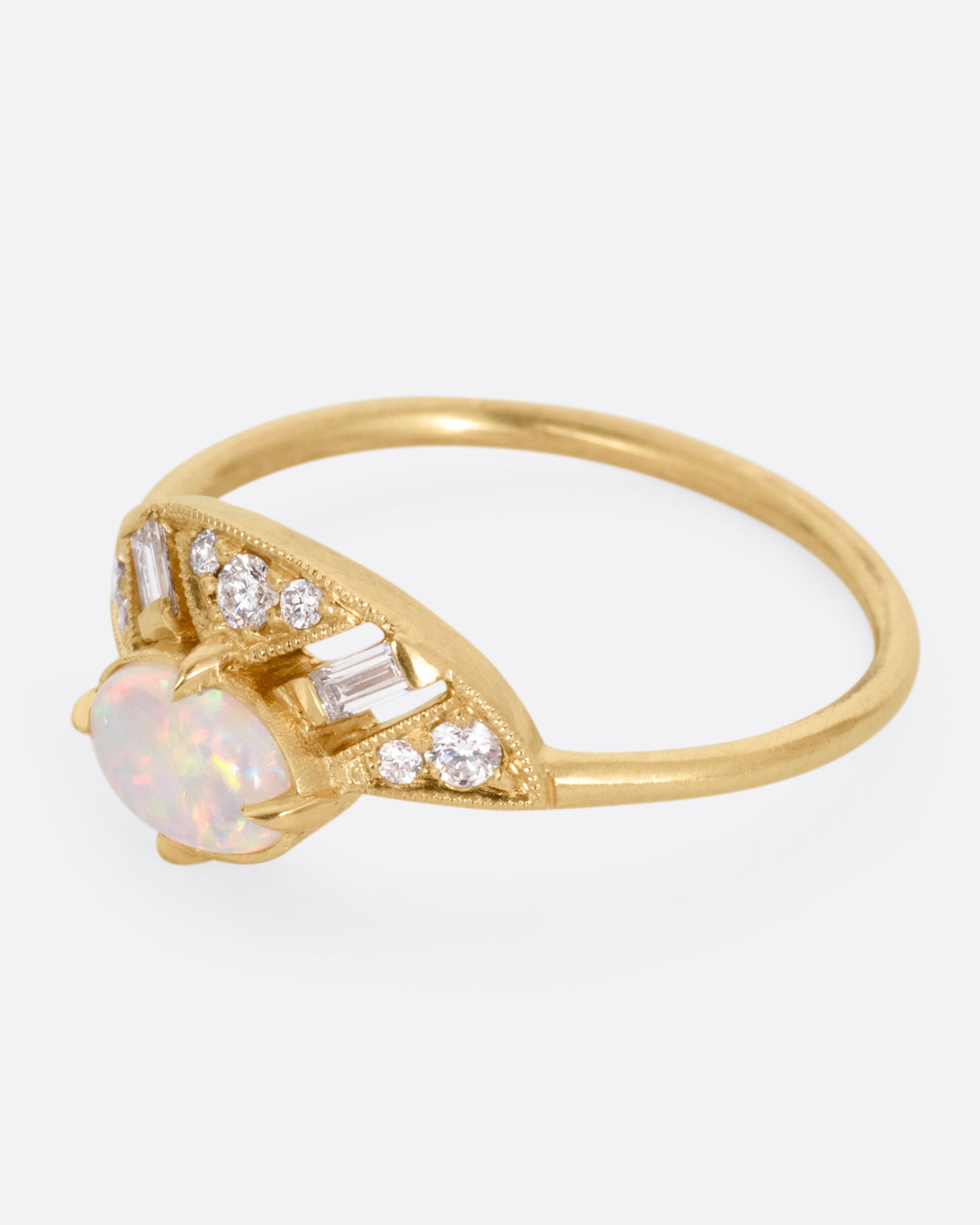 A yellow gold ring with a prong set opal and a diamond studded halo, shown from the side.