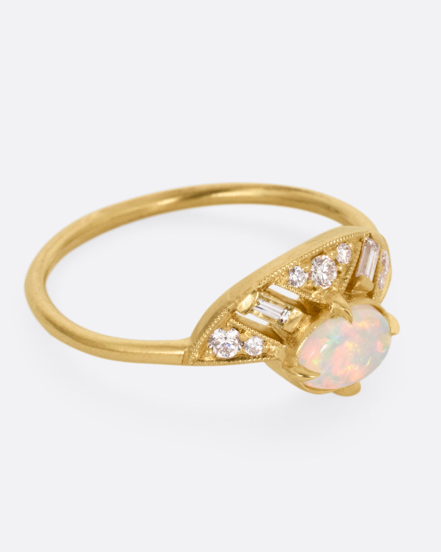A yellow gold ring with a prong set opal and a diamond studded halo, shown from the side.