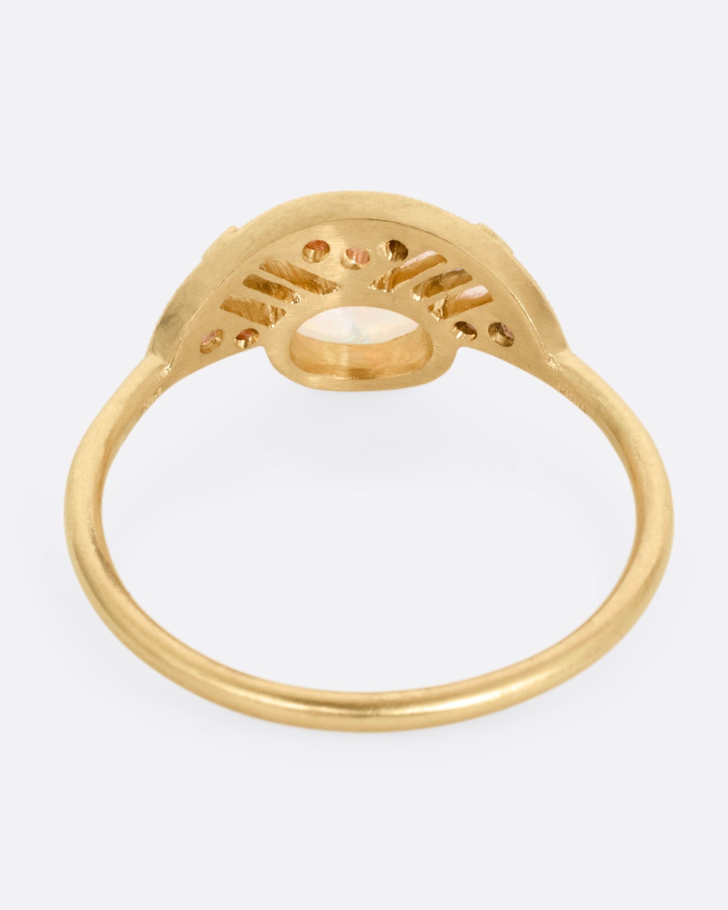 A yellow gold ring with a prong set opal and a diamond studded halo, shown from the back.