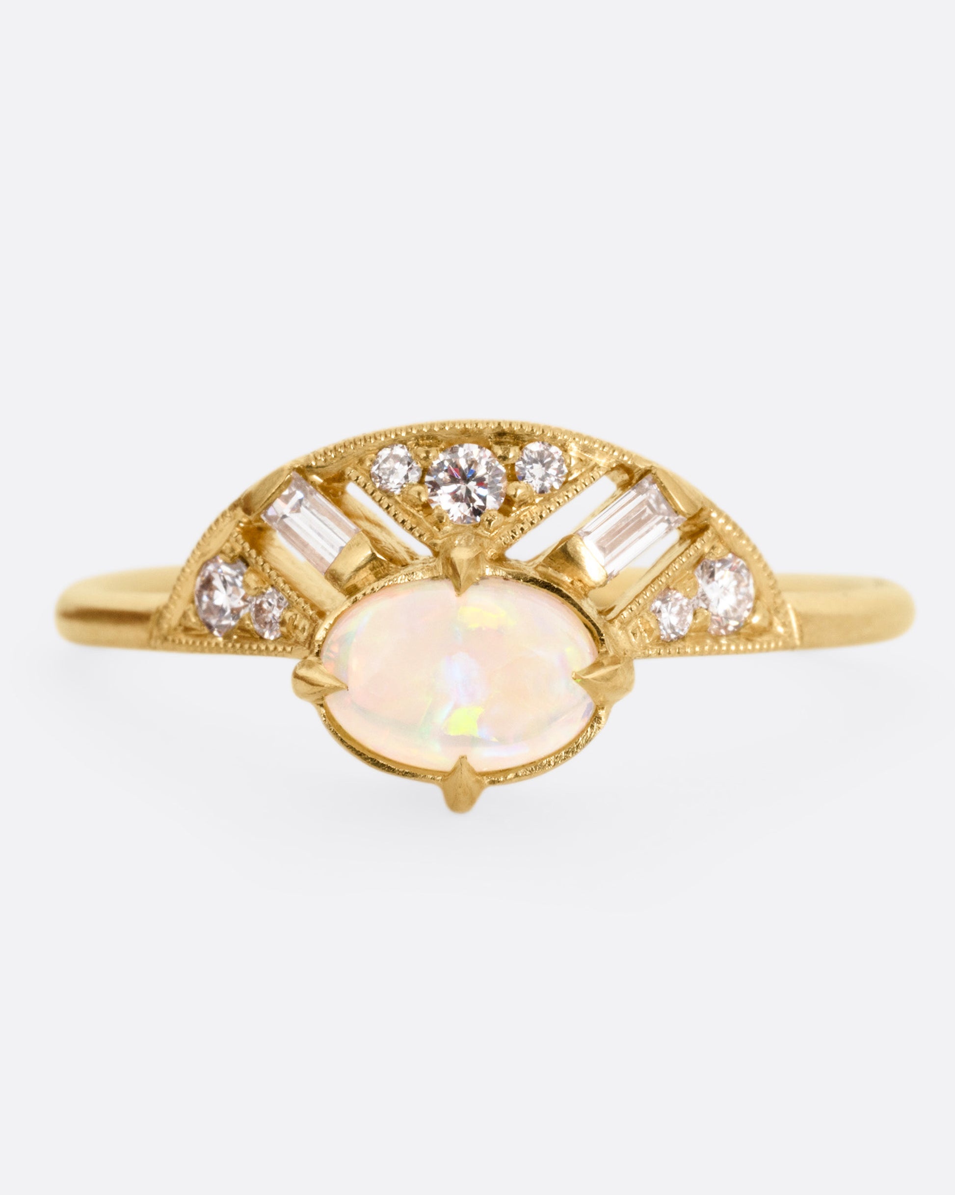 A yellow gold ring with a prong set opal and a diamond studded halo, shown from the front.