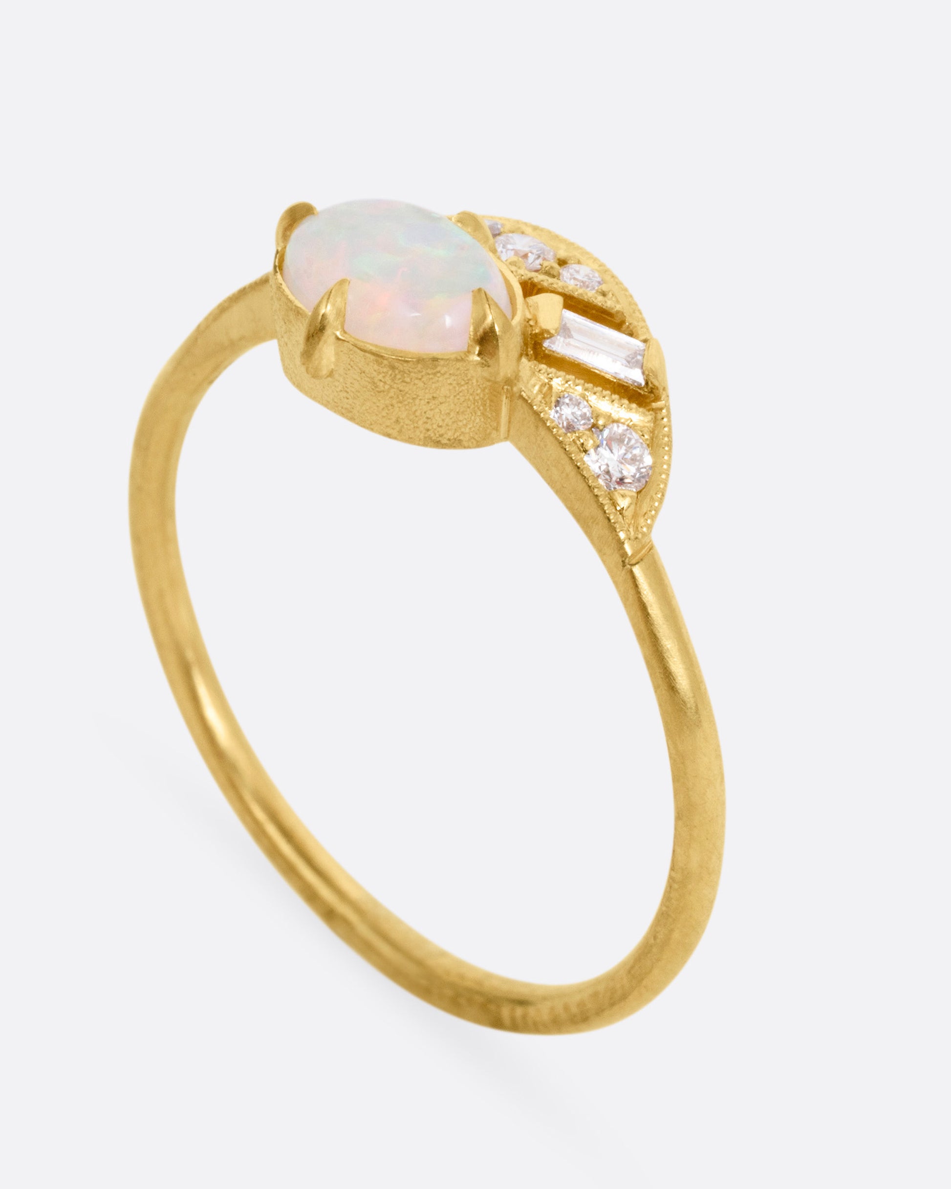 A yellow gold ring with a prong set opal and a diamond studded halo, shown standing up from the side.