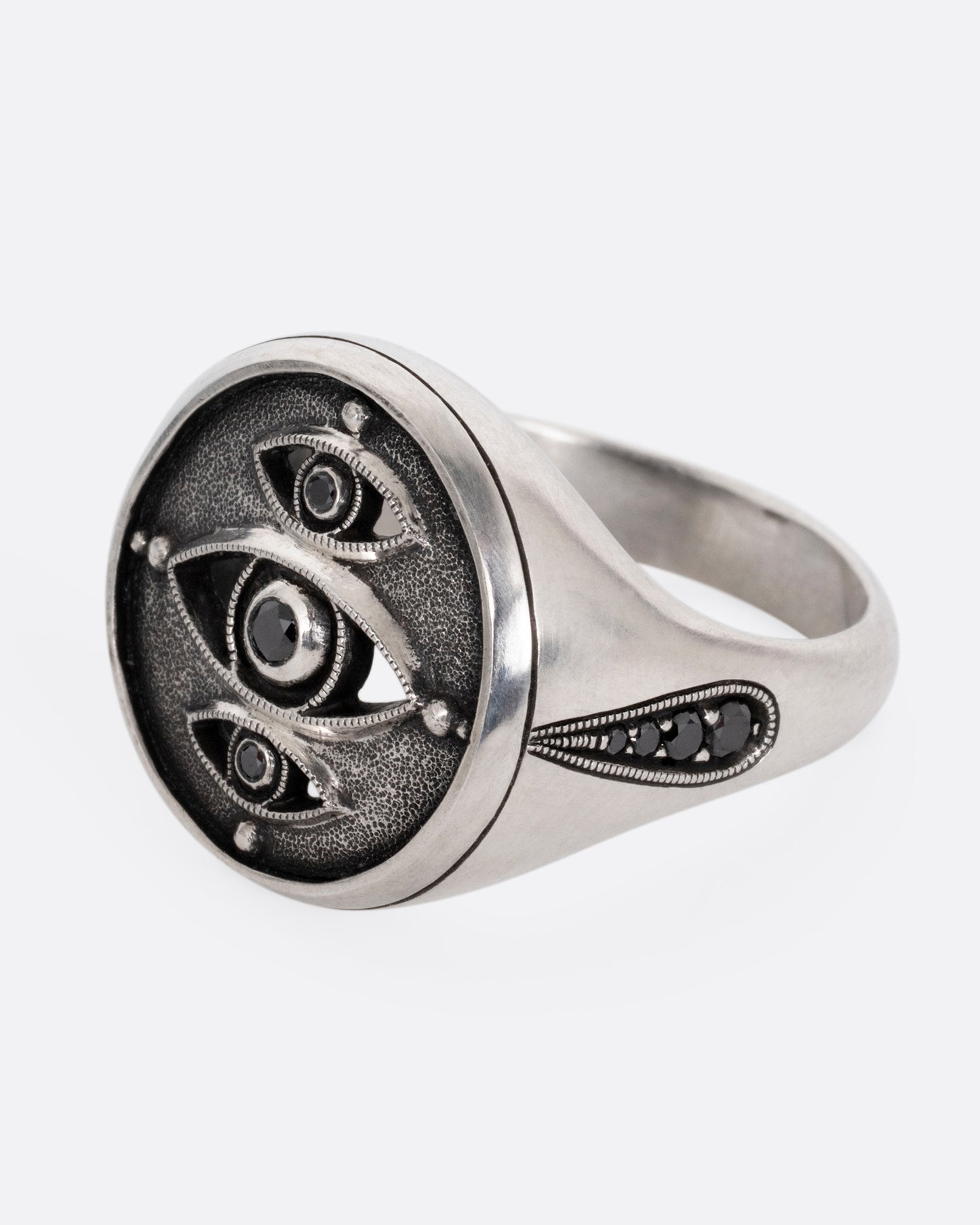 A silver ring with three eyes with black diamond centers, shown from the side.