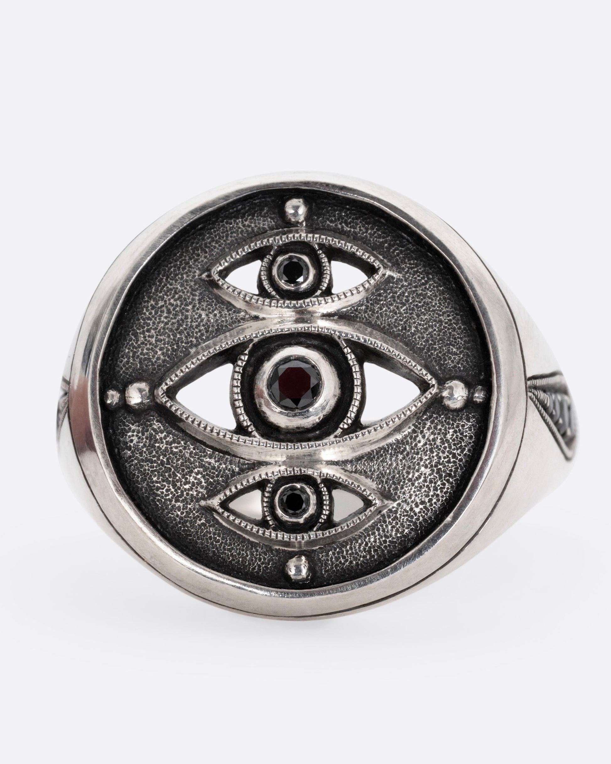 A silver ring with three eyes with black diamond centers, shown from the front.