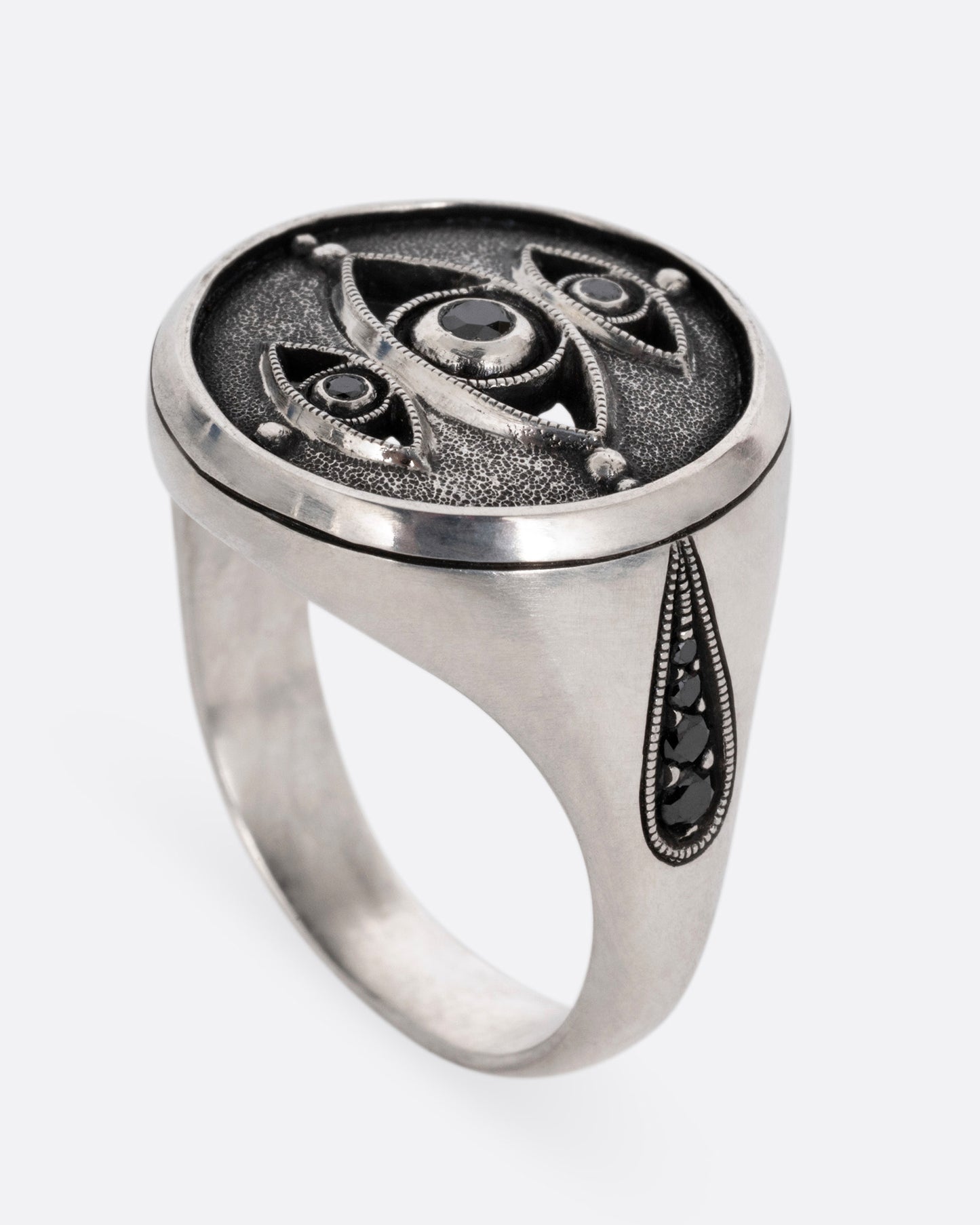 A silver ring with three eyes with black diamond centers, shown from the side standing up.