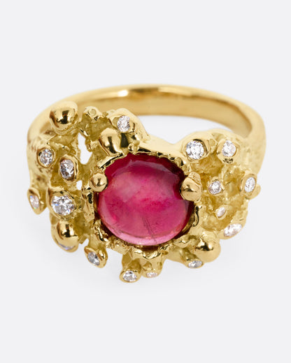A yellow gold ring with a bed of diamond tipped anemones, and a red rubellite, shown from the front.