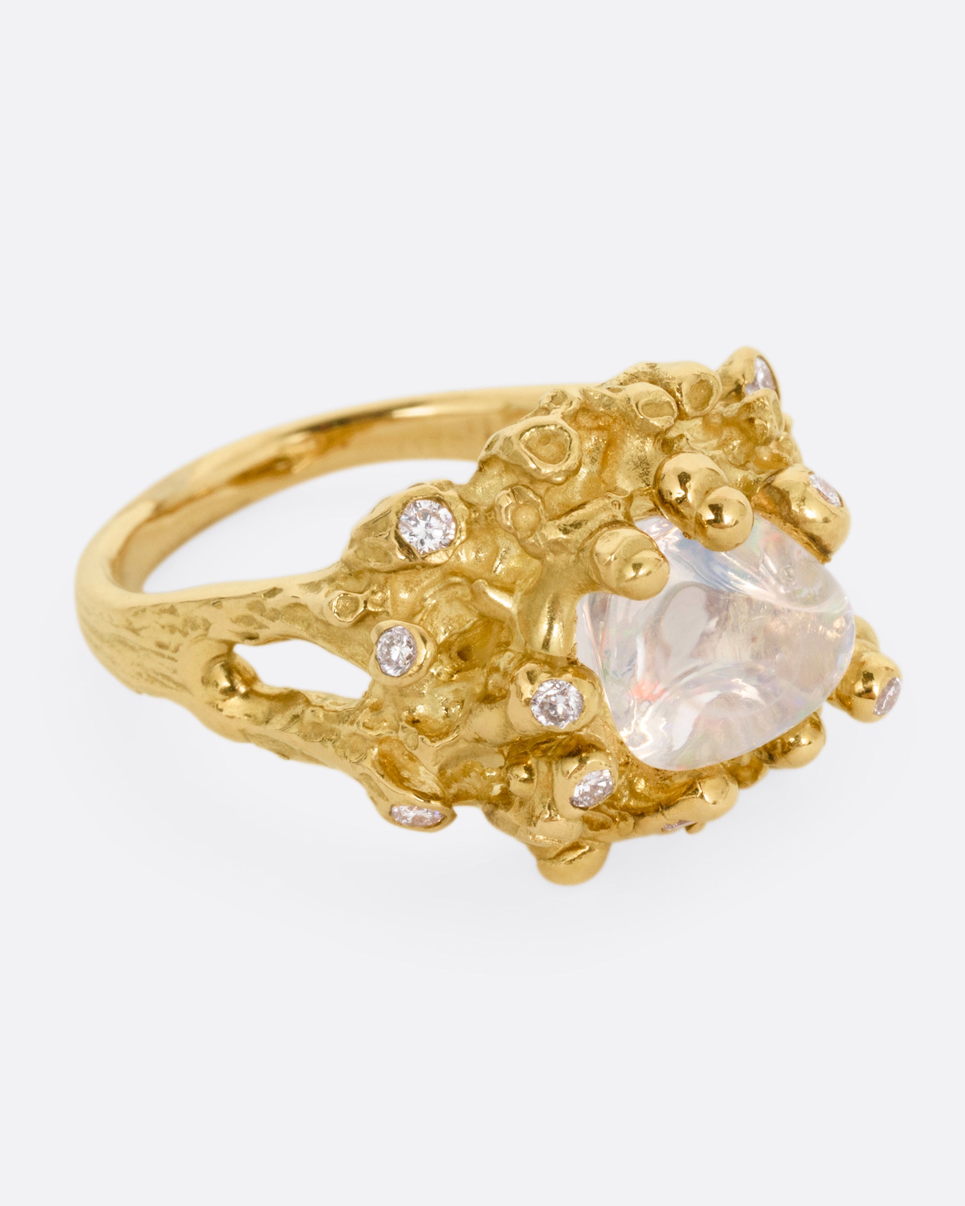 A yellow gold ring with a dimensional nest-like setting studded with diamonds and an opal, shown from the side.