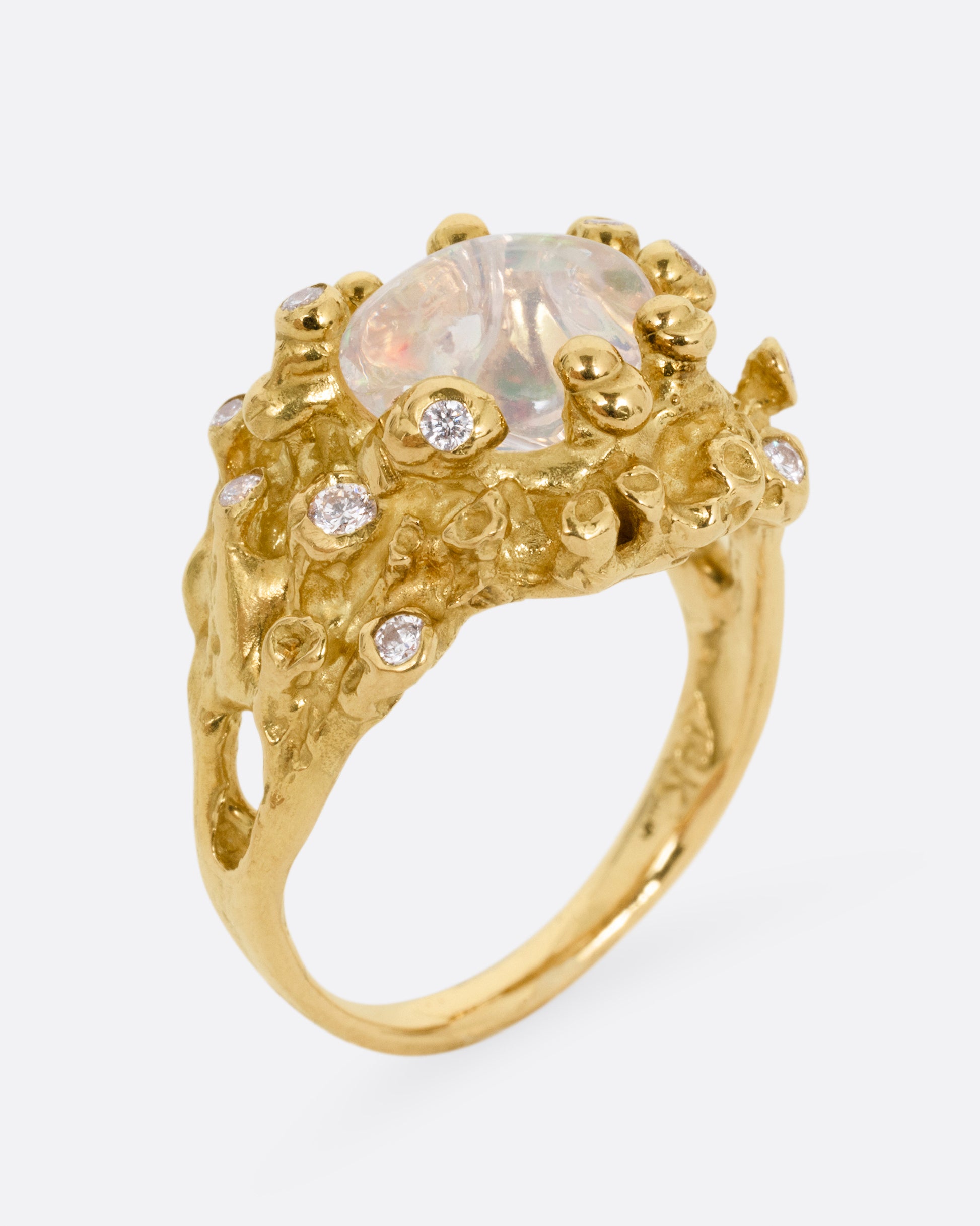 A yellow gold ring with a dimensional nest-like setting studded with diamonds and an opal, shown standing up from the side.