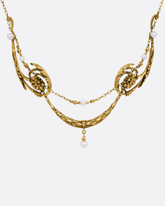 A yellow gold necklace with pearls and flower details, shown from the front.