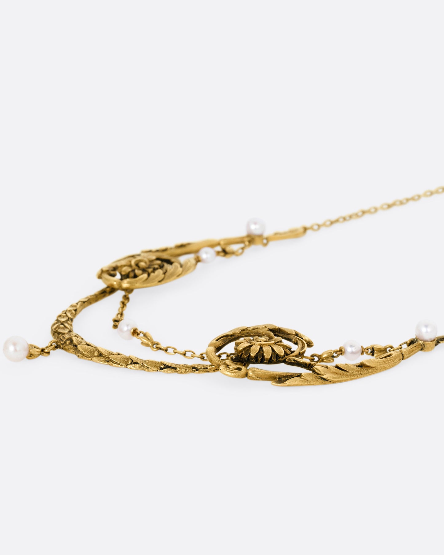 A yellow gold necklace with pearls and flower details, shown from the side.