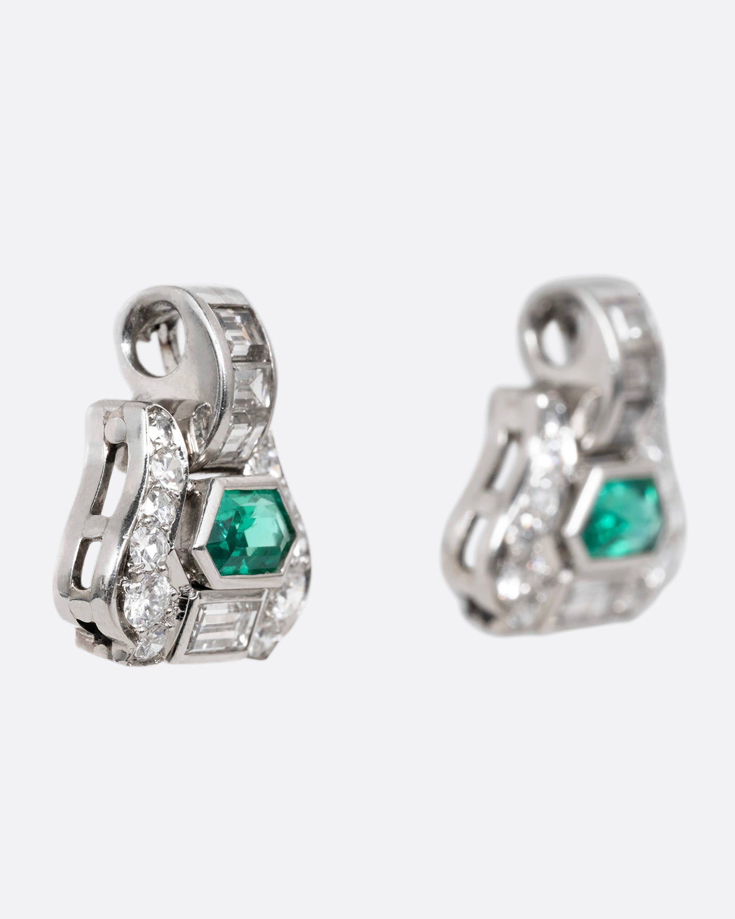 A pair of platinum earrings with emeralds and diamonds, shown from the side.