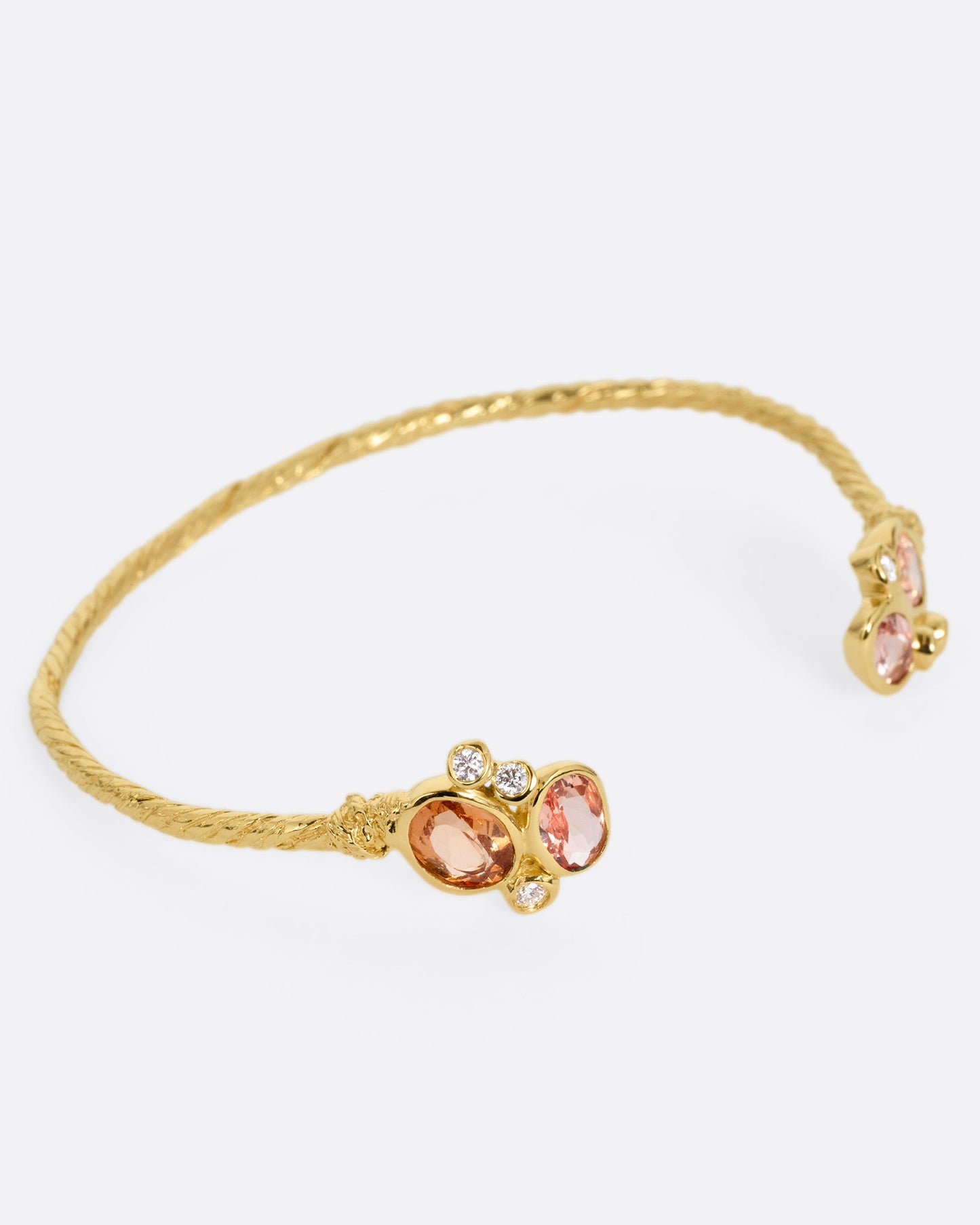 A yellow gold hand carved cuff bracelet with clusters of tourmalines and diamonds on either side of its open front, shown from the side.